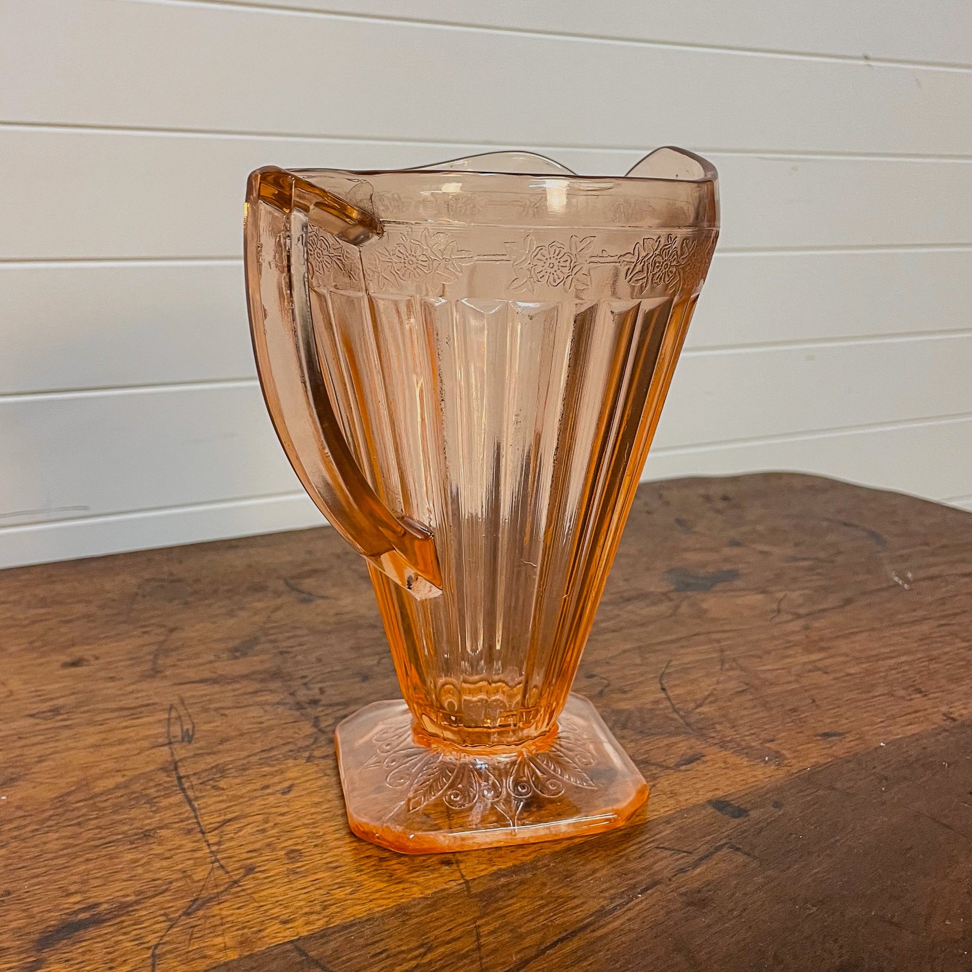 Decorative amber glass vase on a wooden surface with a white paneled background