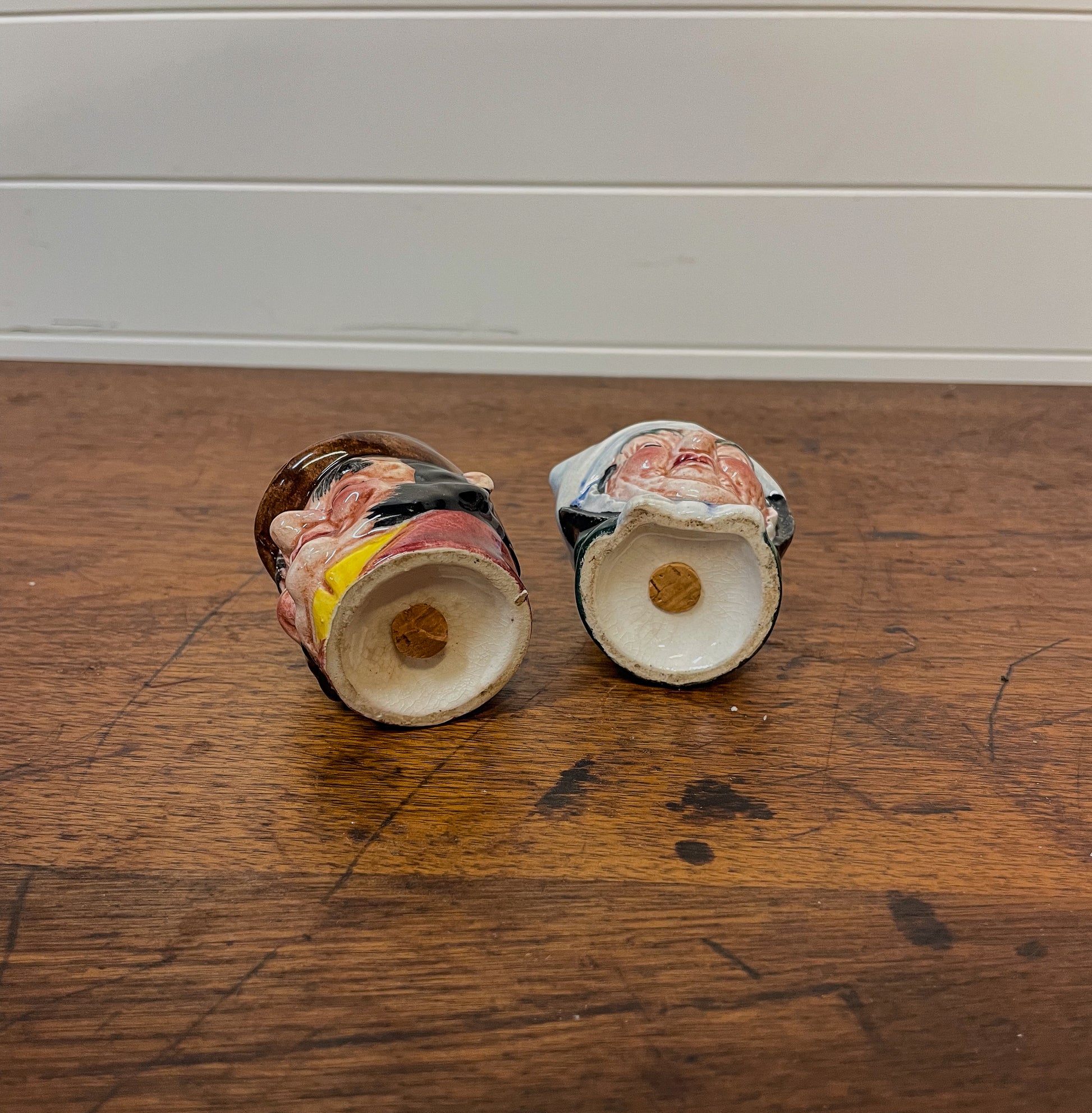 Two ceramic salt and pepper shakers on a wooden surface with a neutral background