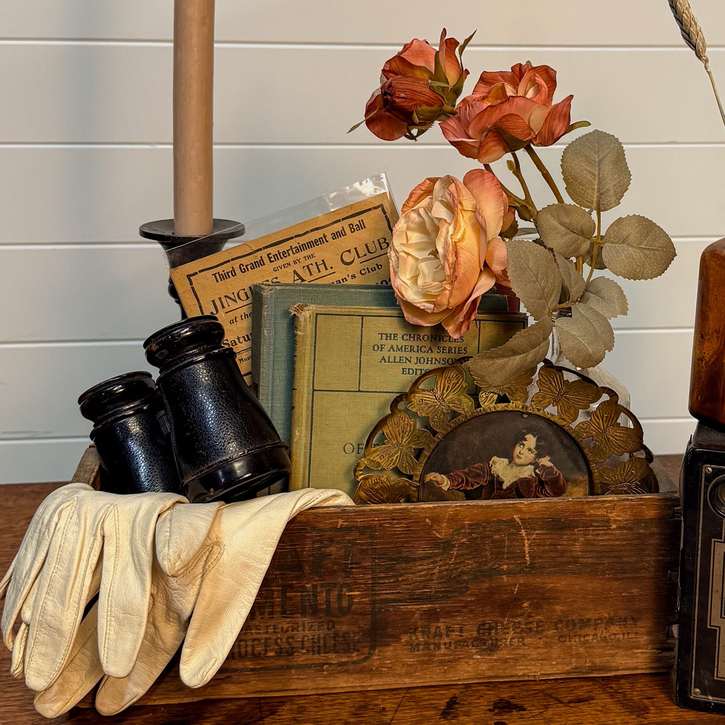 Vintage-style arrangement with a candle, books, gloves, and bottles on a wooden surface.