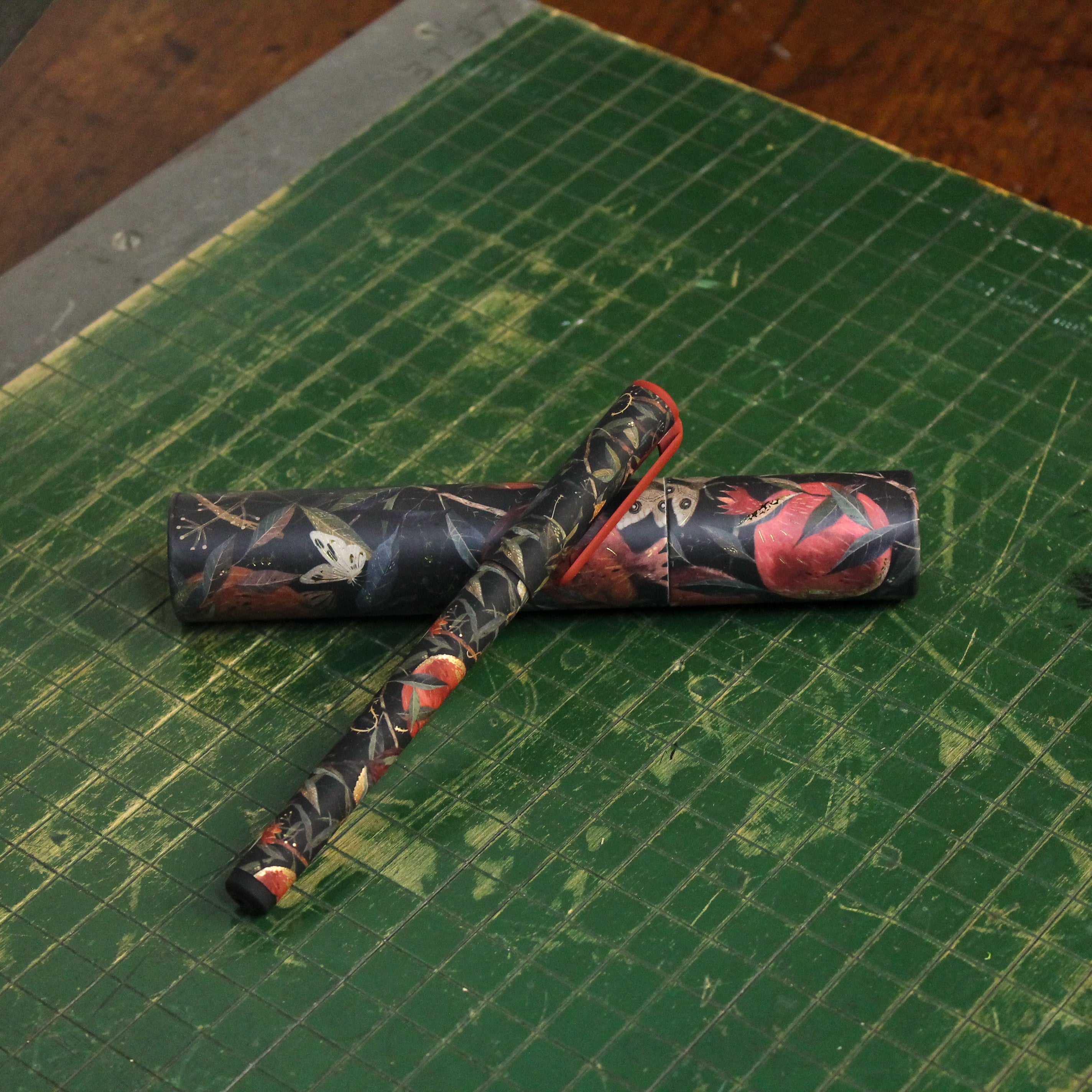 A pen sitting on top of its tubed case on a green cutting board