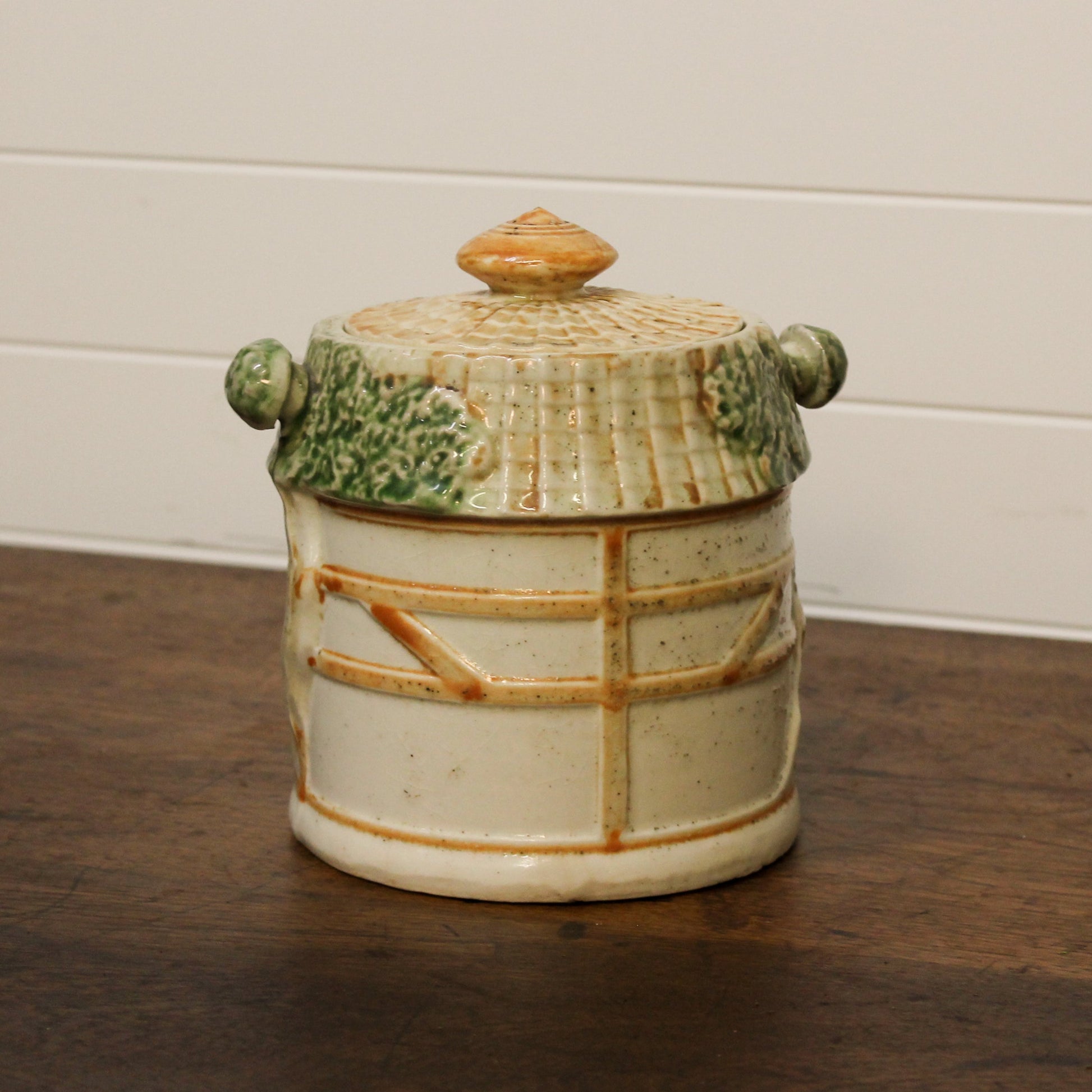 Ceramic jar with lid on a wooden surface against a white wall