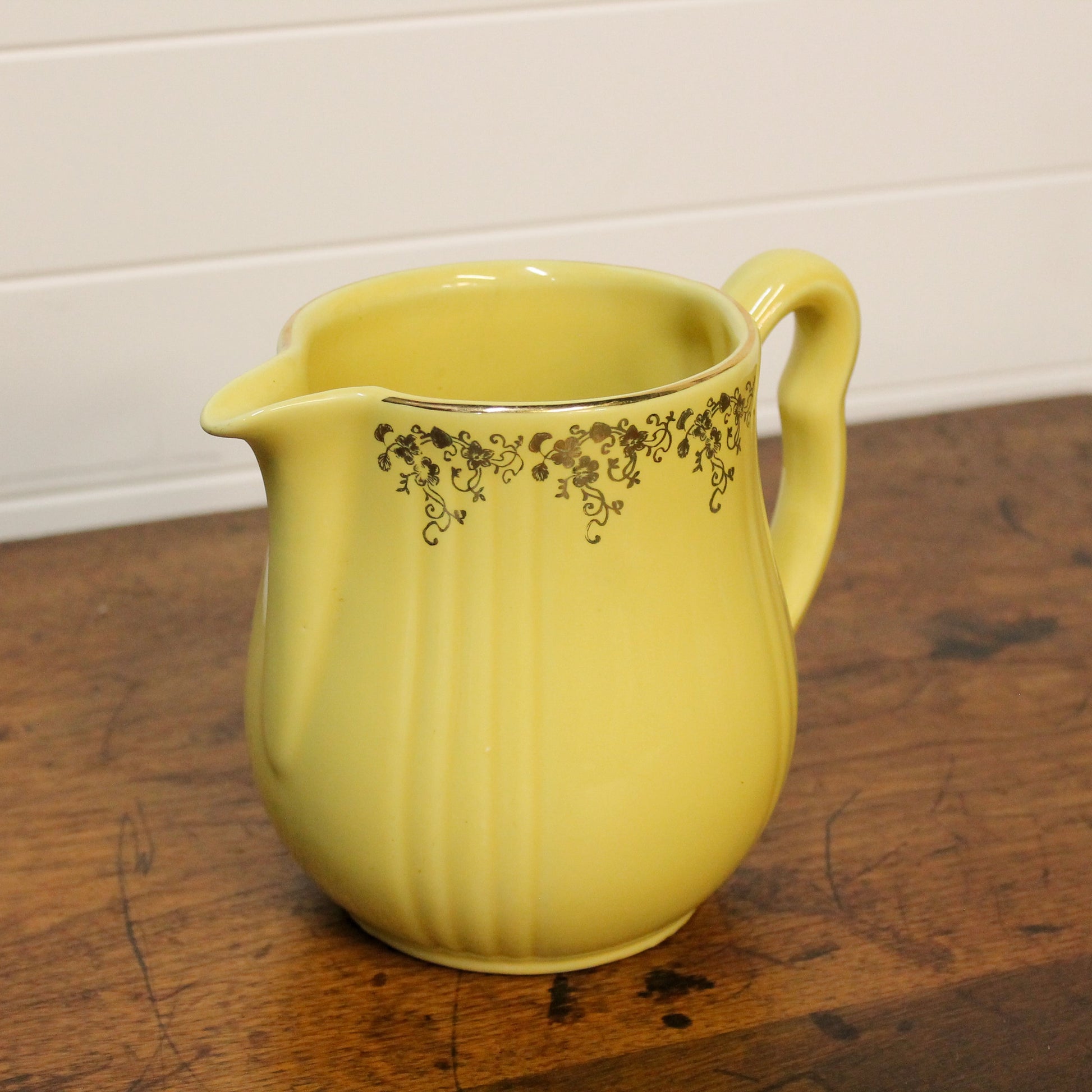 Yellow ceramic pitcher with floral patterns on a wooden surface