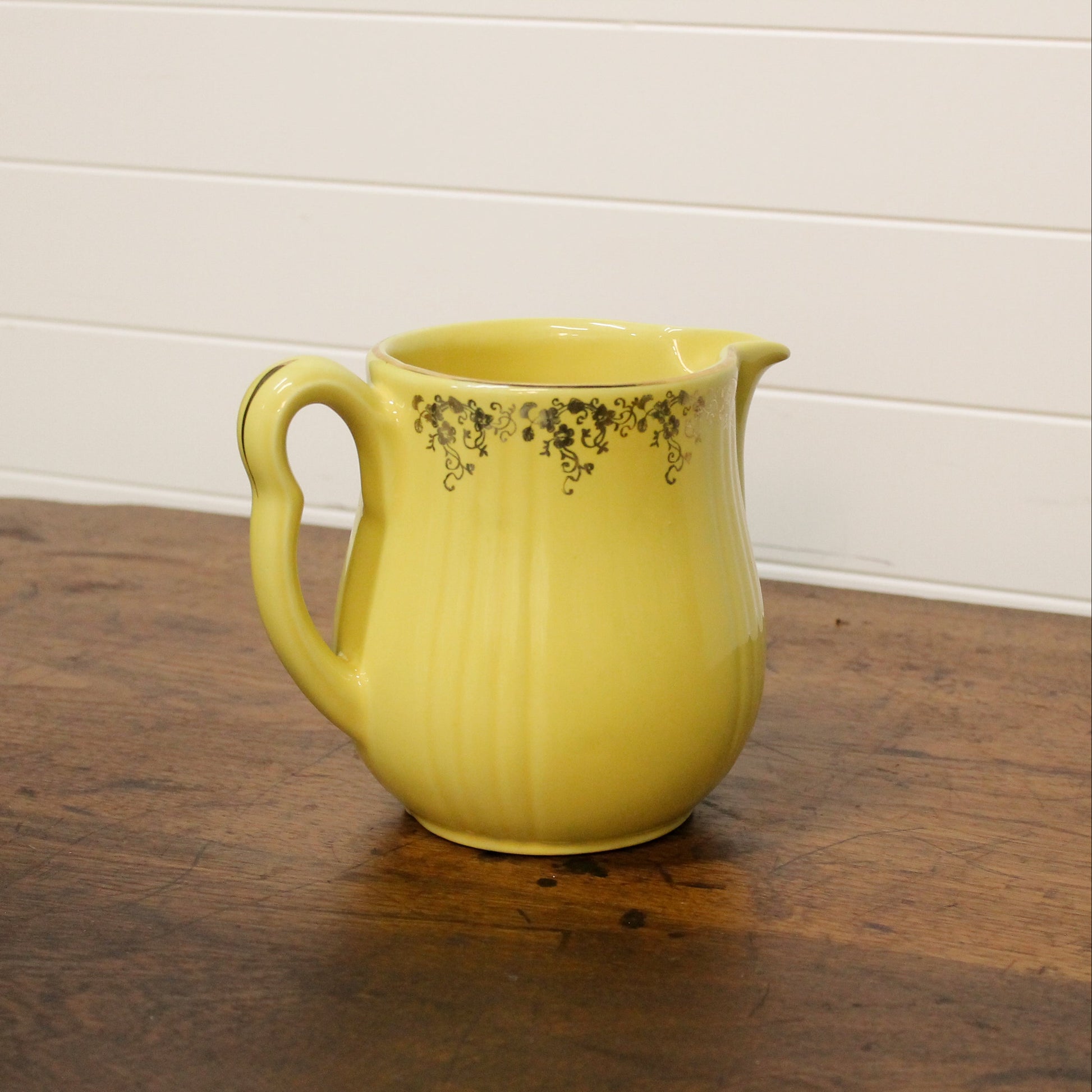 Yellow ceramic pitcher on a wooden surface with a white wall background
