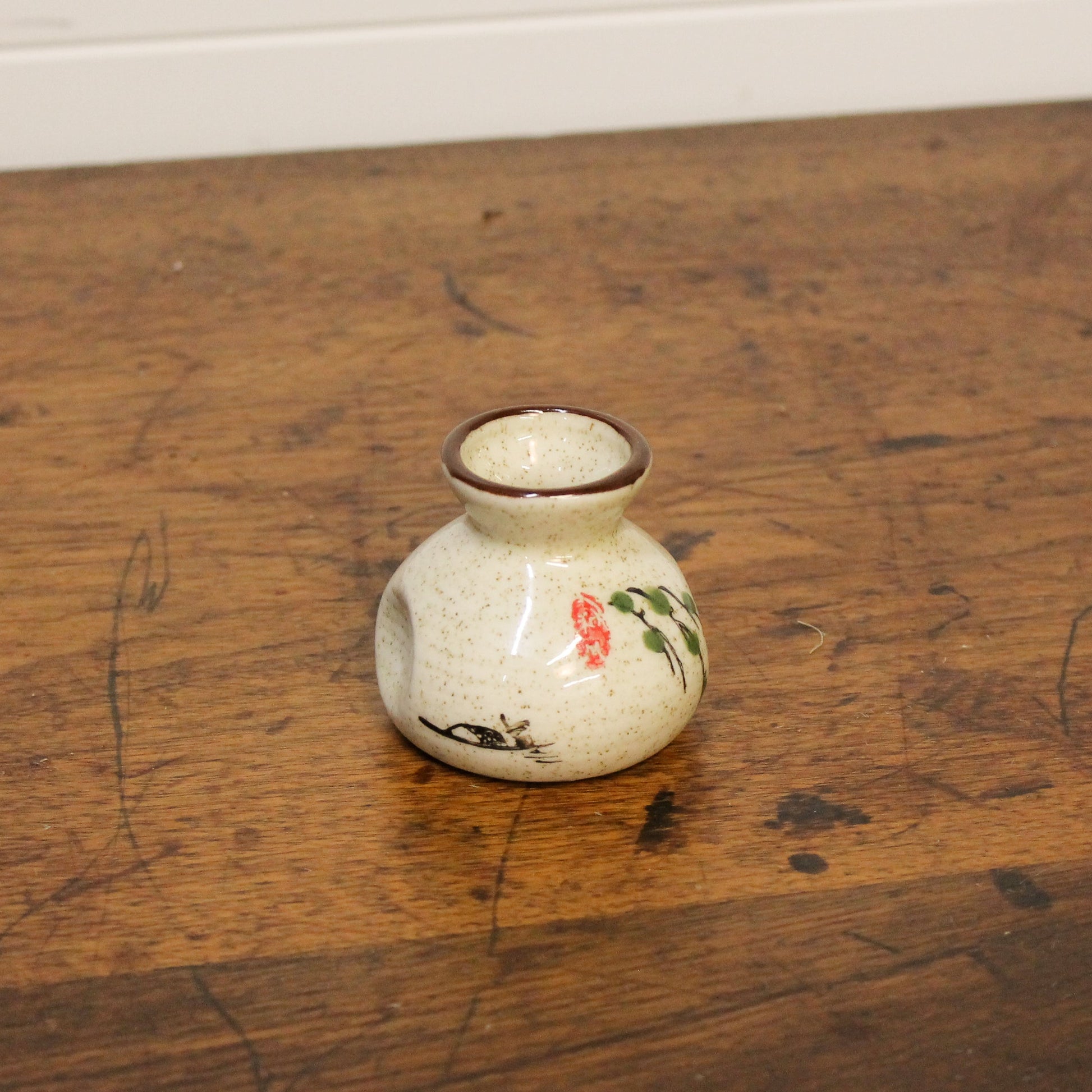 Small ceramic vase with floral designs on a wooden floor
