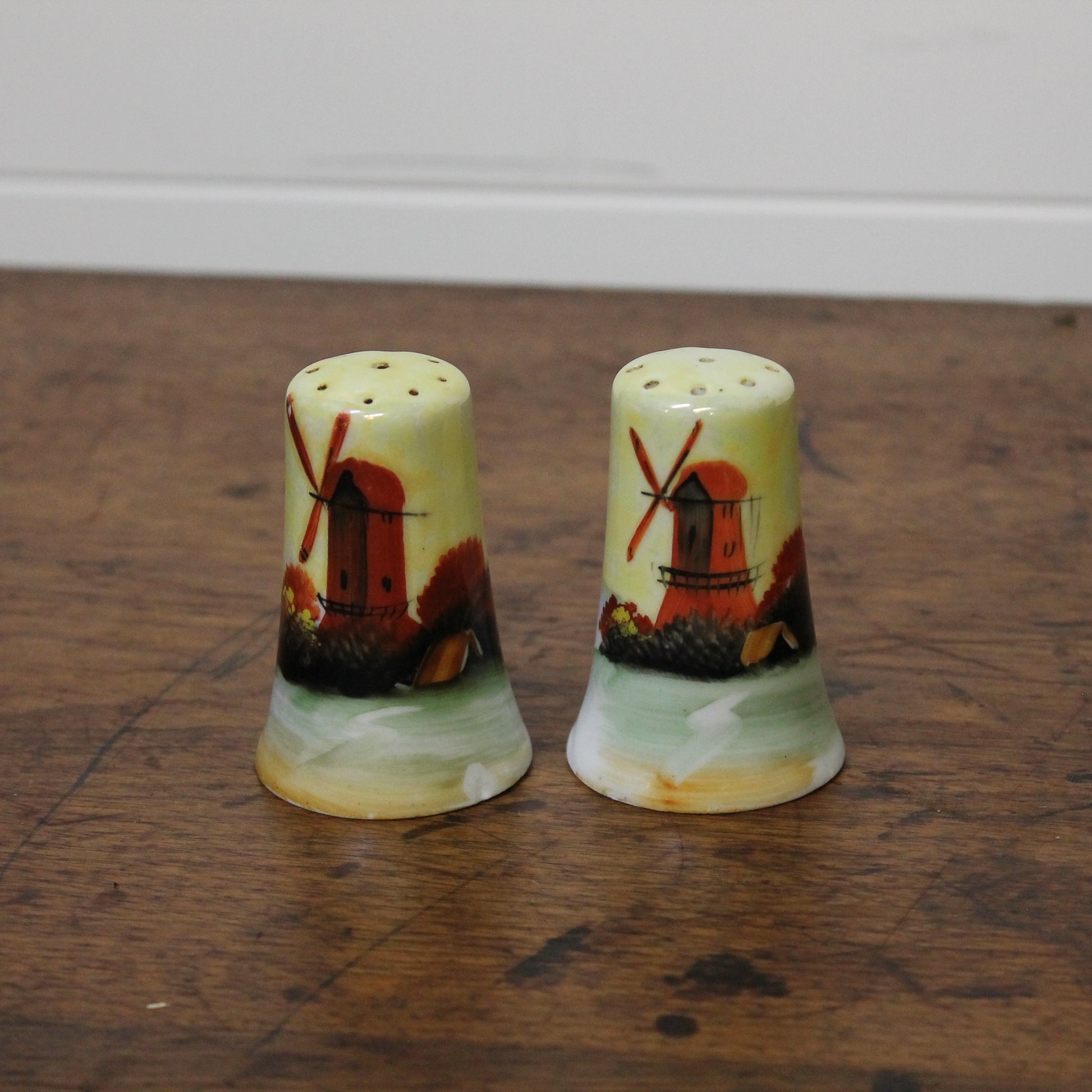 Two ceramic salt and pepper shakers with windmill design on a wooden surface.