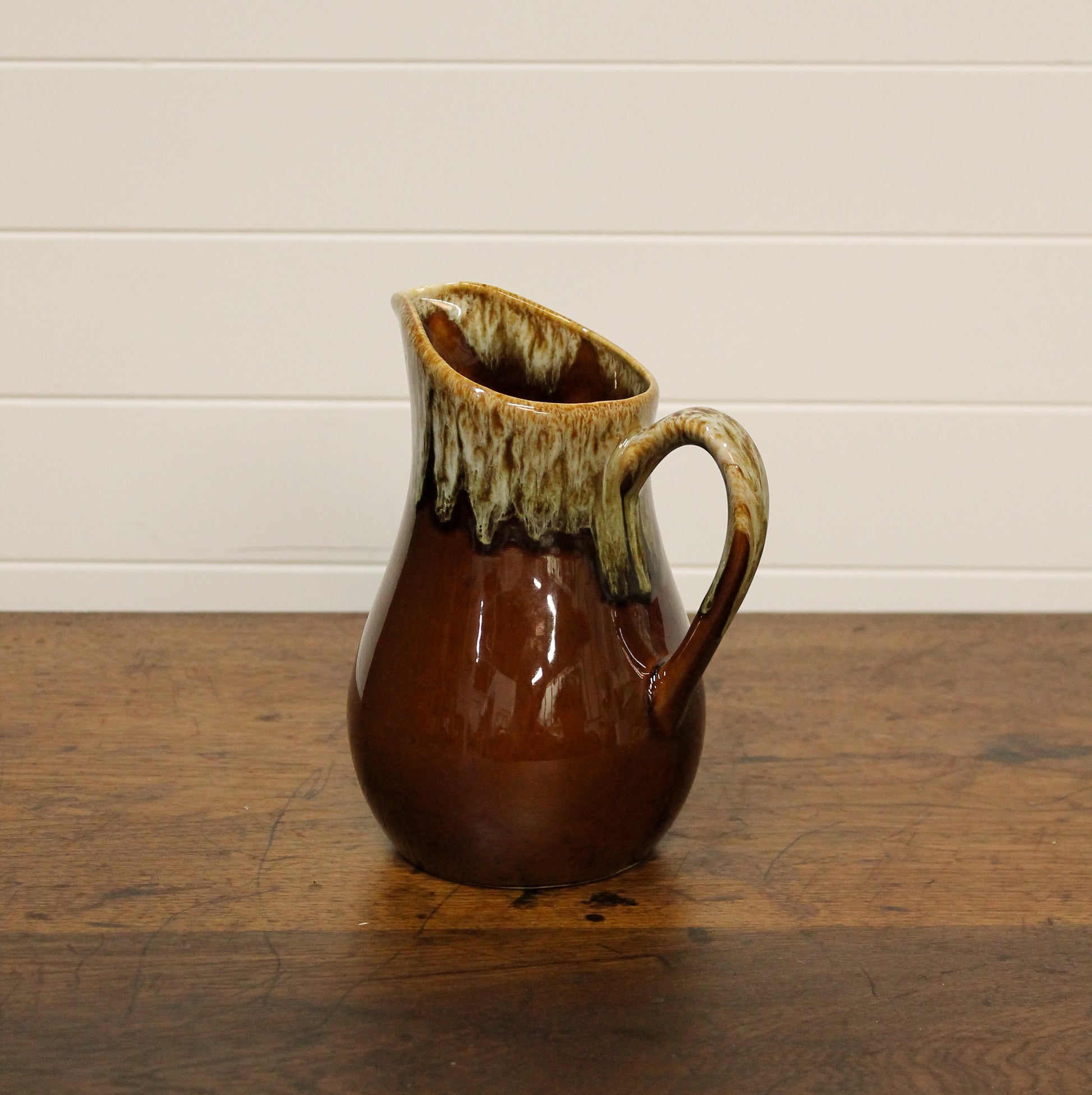 Brown ceramic pitcher with a greenish top on a wooden surface