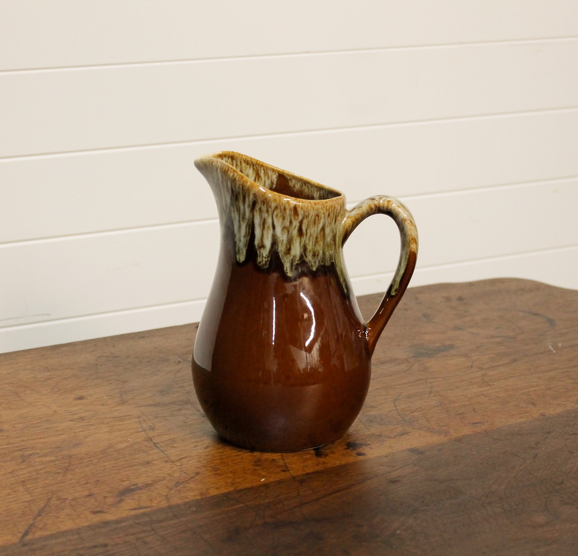 Brown ceramic pitcher on a wooden surface with a white wall background