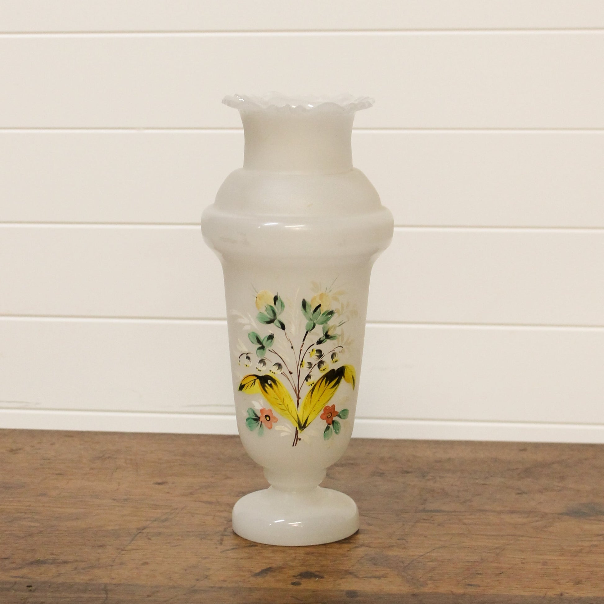 White vase with floral design on a wooden surface and white wall background