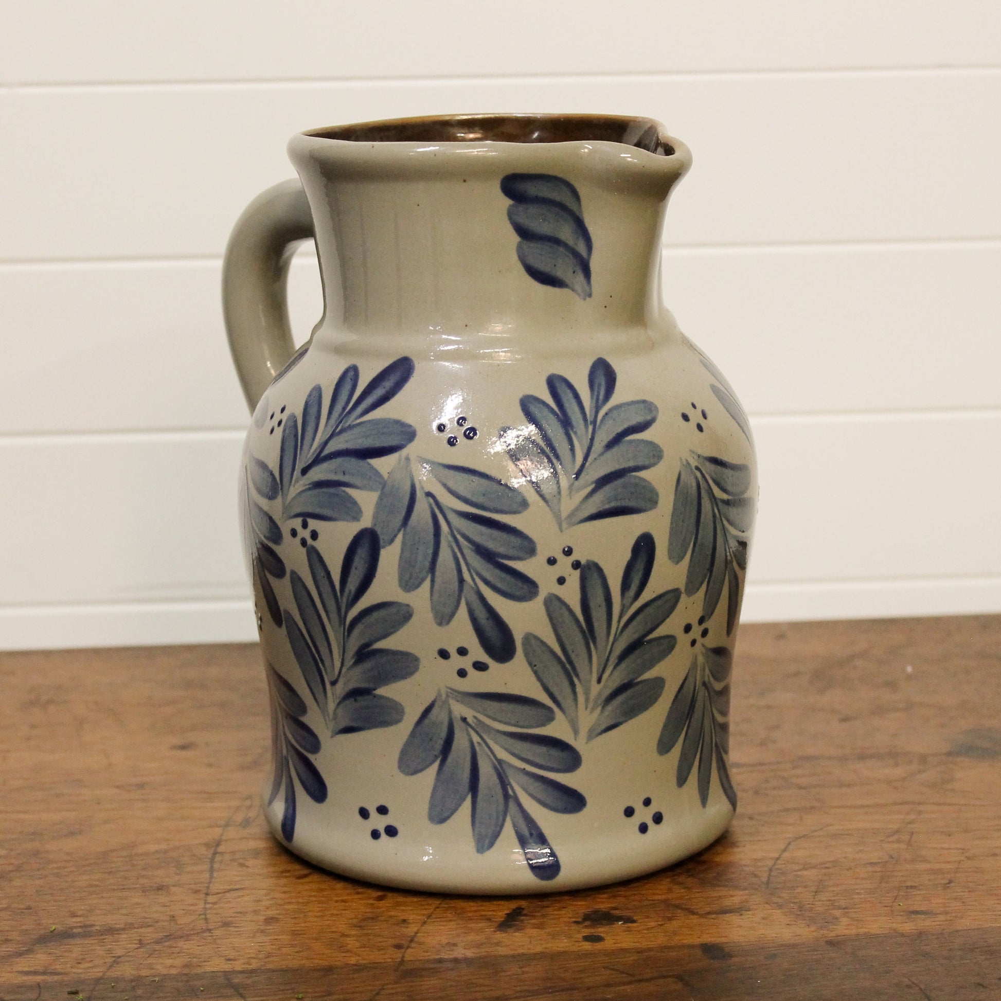 Ceramic pitcher with blue leaf patterns on a wooden surface