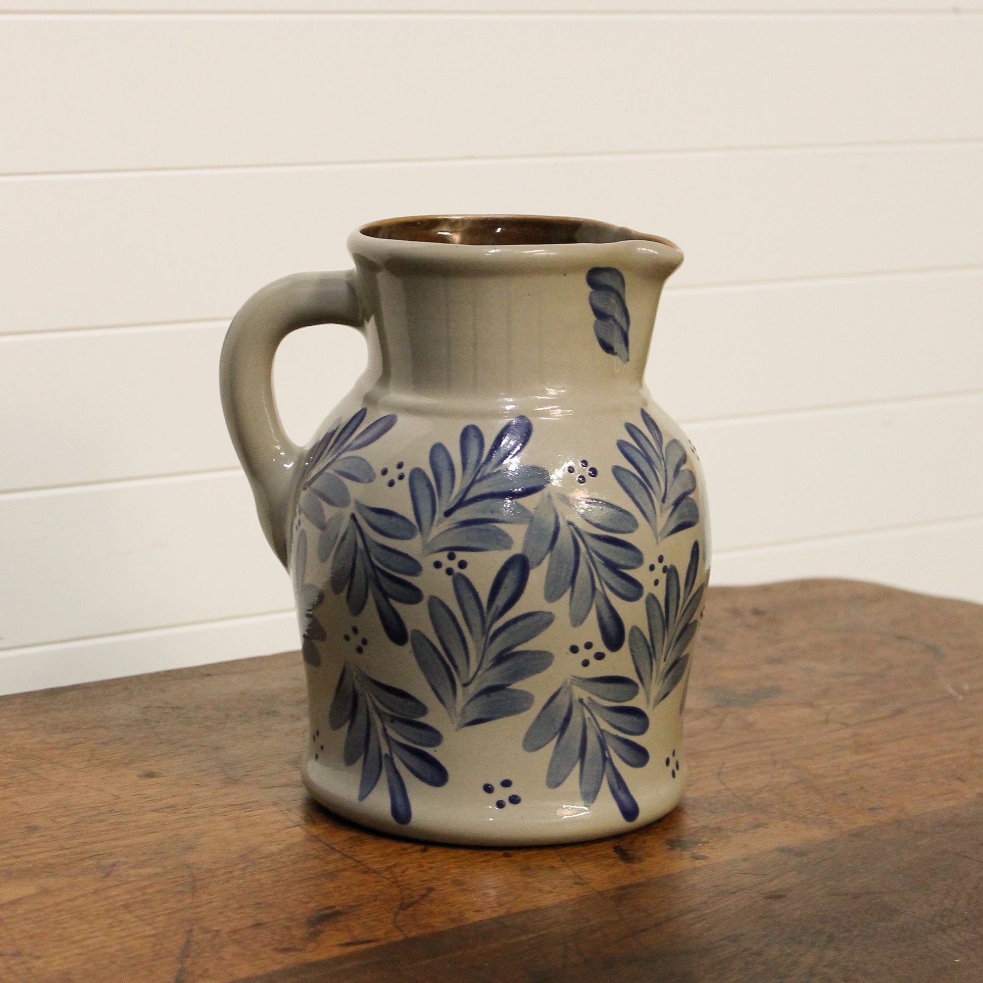 Ceramic pitcher with blue floral patterns on a wooden surface and white wall background