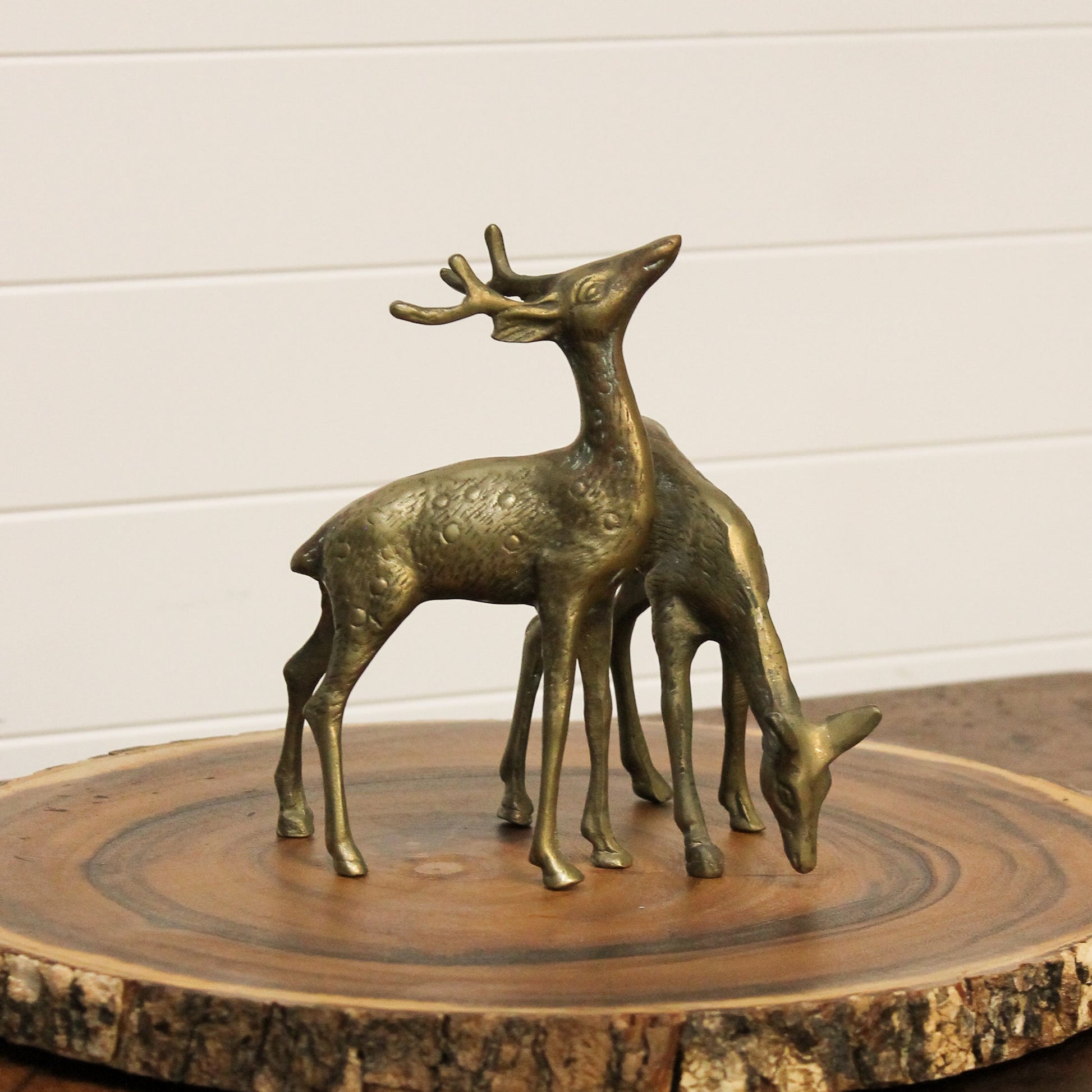 Brass deer figurines on a wooden surface with a white wall background