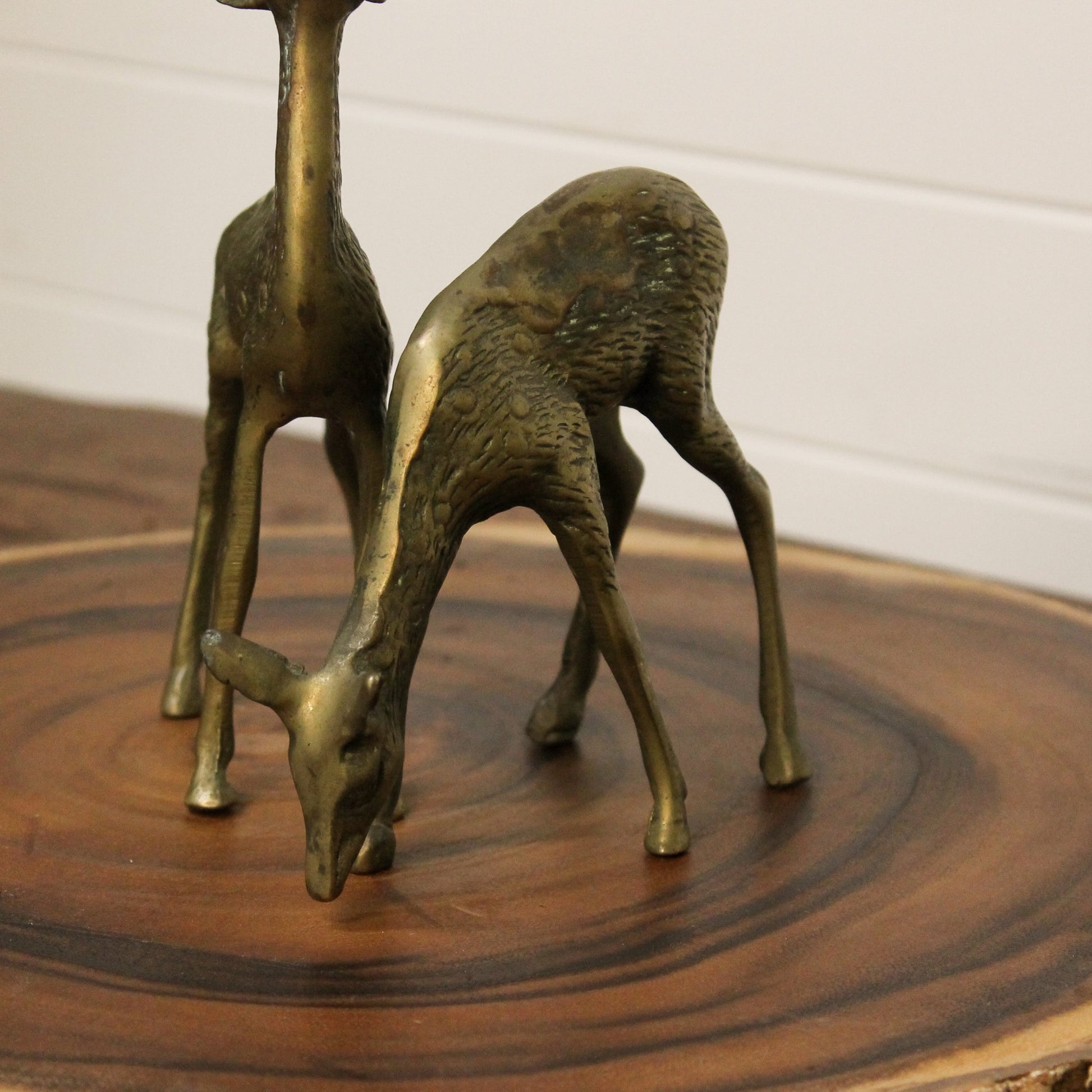 Two brass deer figurines on a wooden surface with a white background