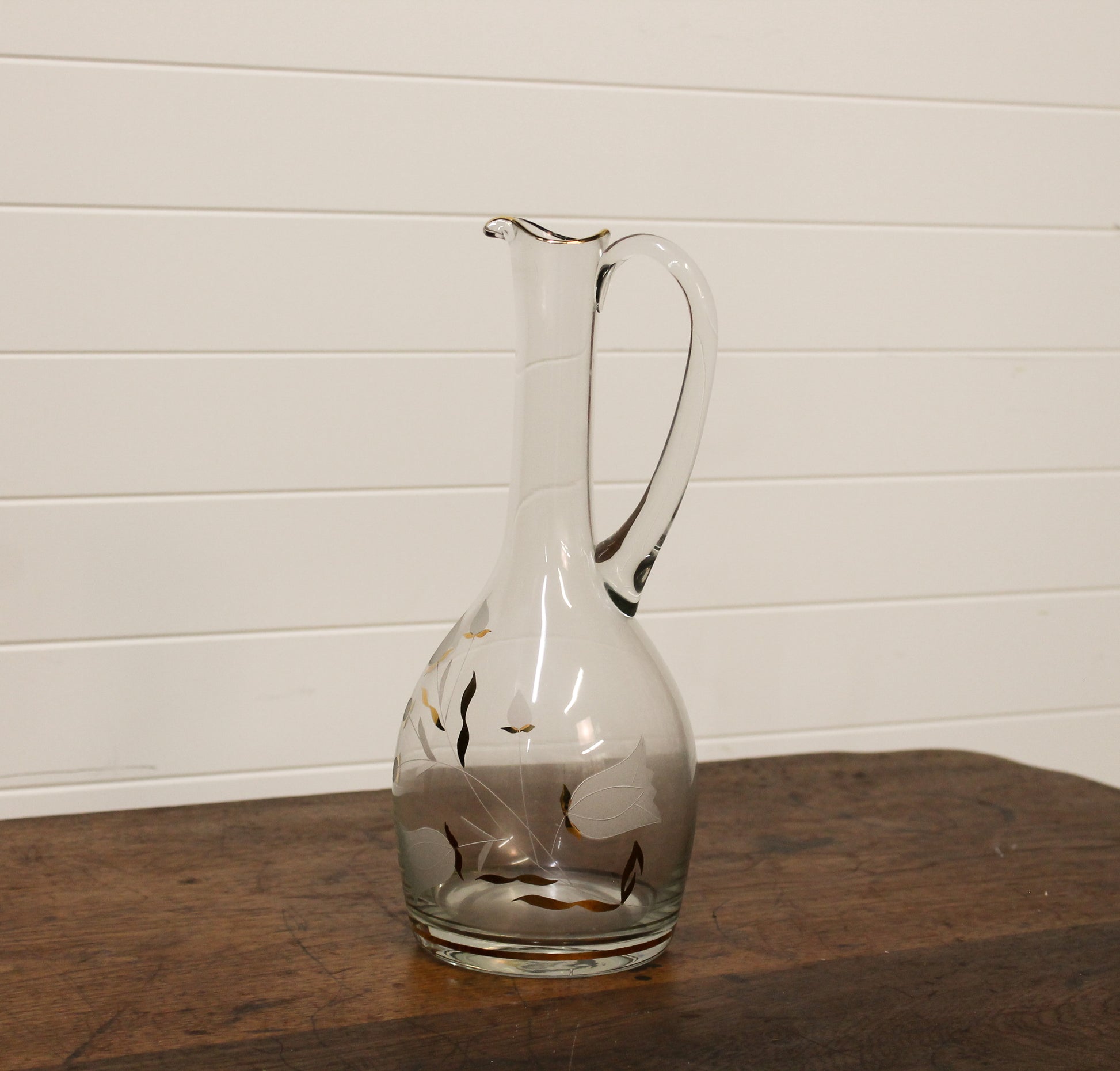 Clear glass decanter with floral etching on a wooden surface and white wall background