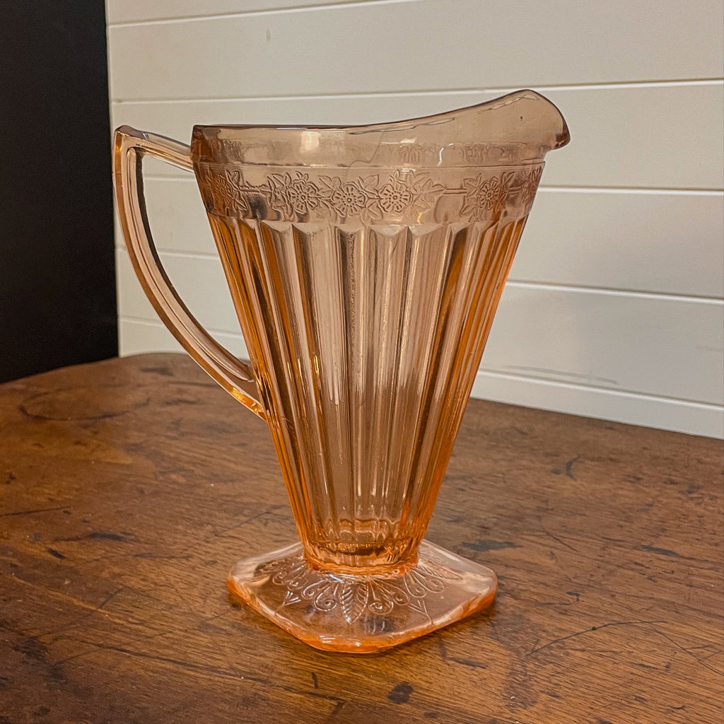 Vintage pink glass pitcher on a wooden surface with a white paneled wall background