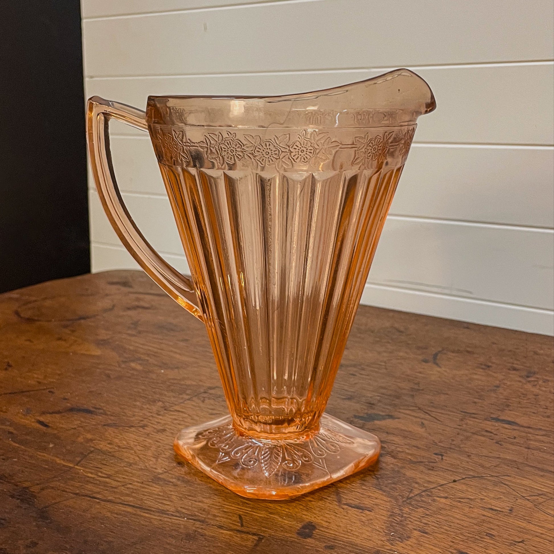 Vintage pink glass pitcher on a wooden surface with a white paneled wall background