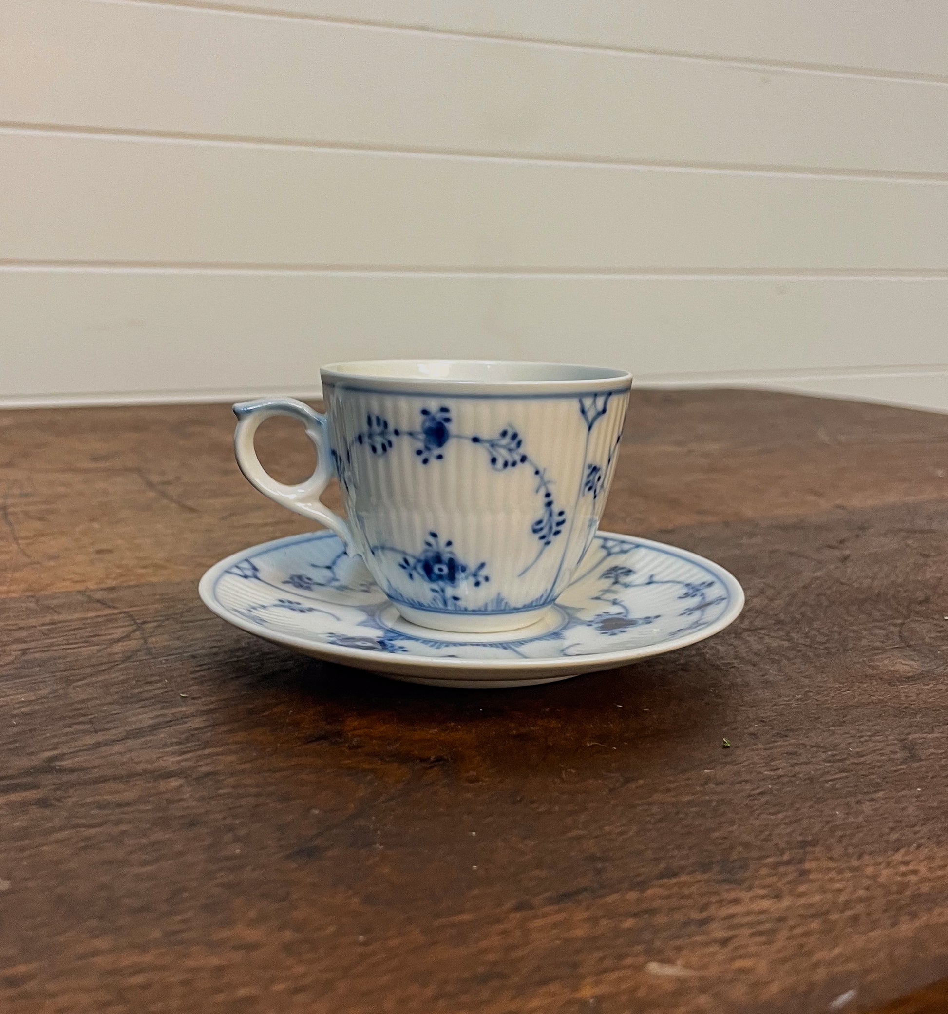 Blue and white floral teacup and saucer on a wooden table with a white wall background