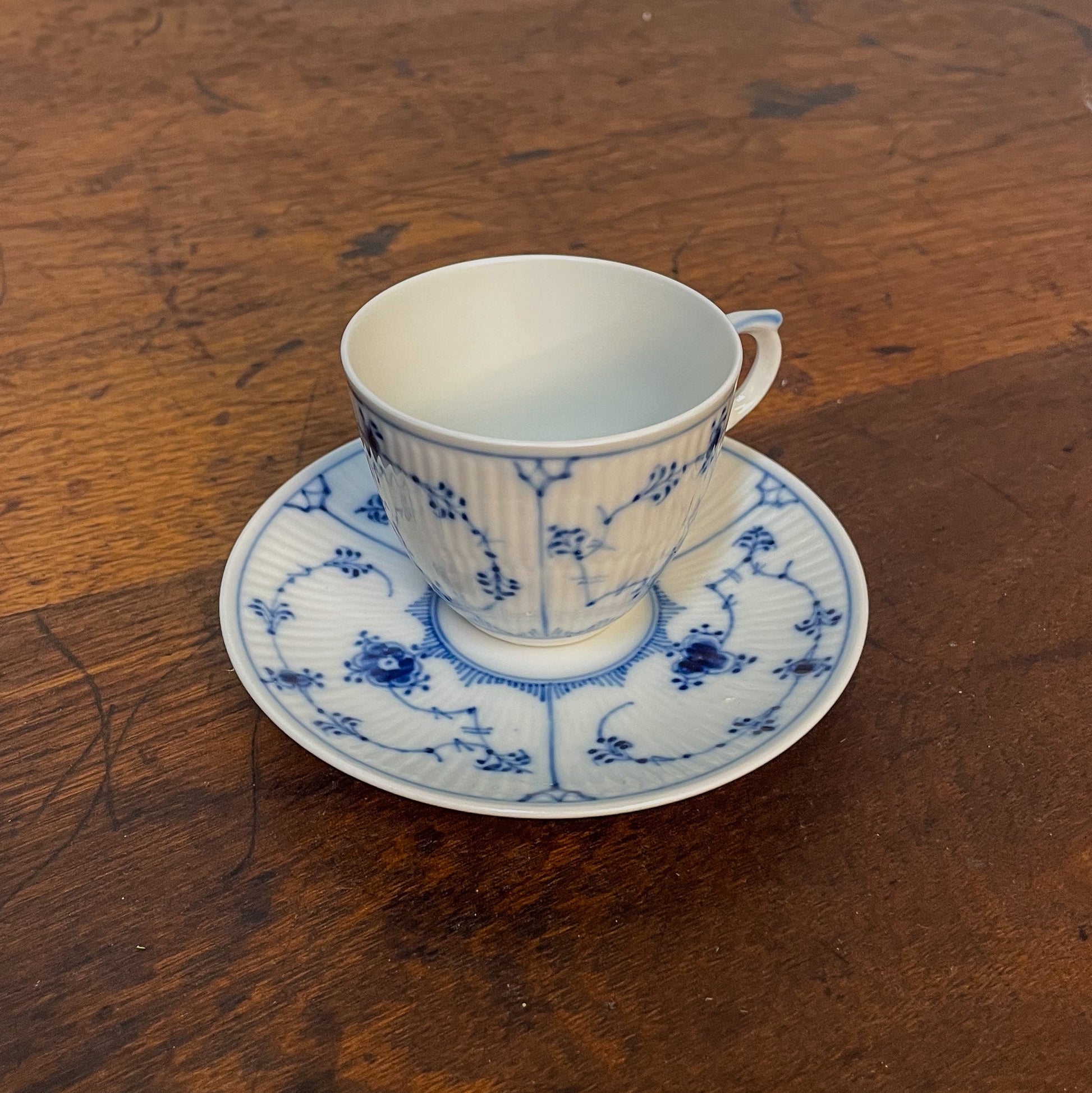 White teacup with blue floral patterns on a matching saucer, placed on a wooden surface.