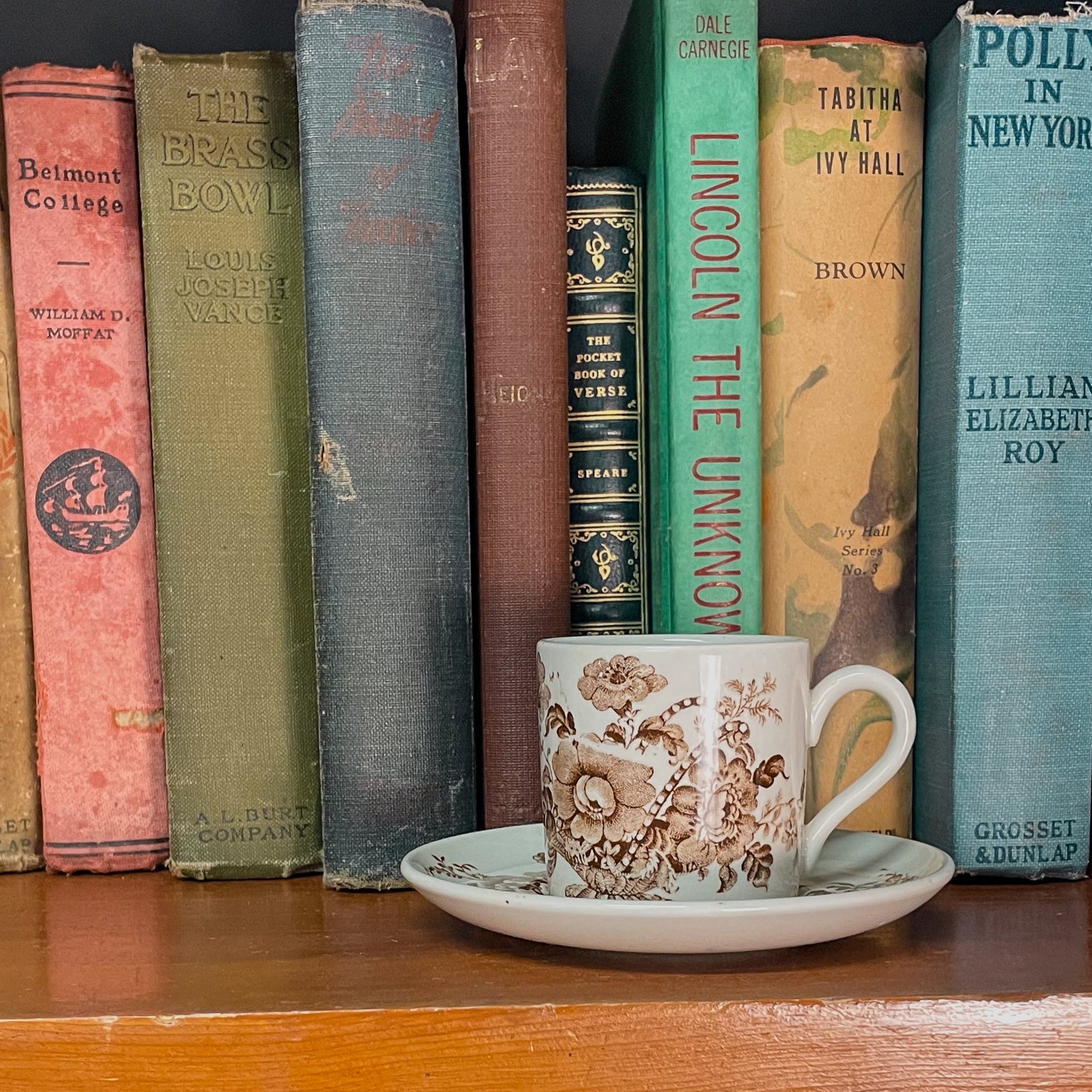 Row of vintage books on a shelf with a decorative cup and saucer in the center.