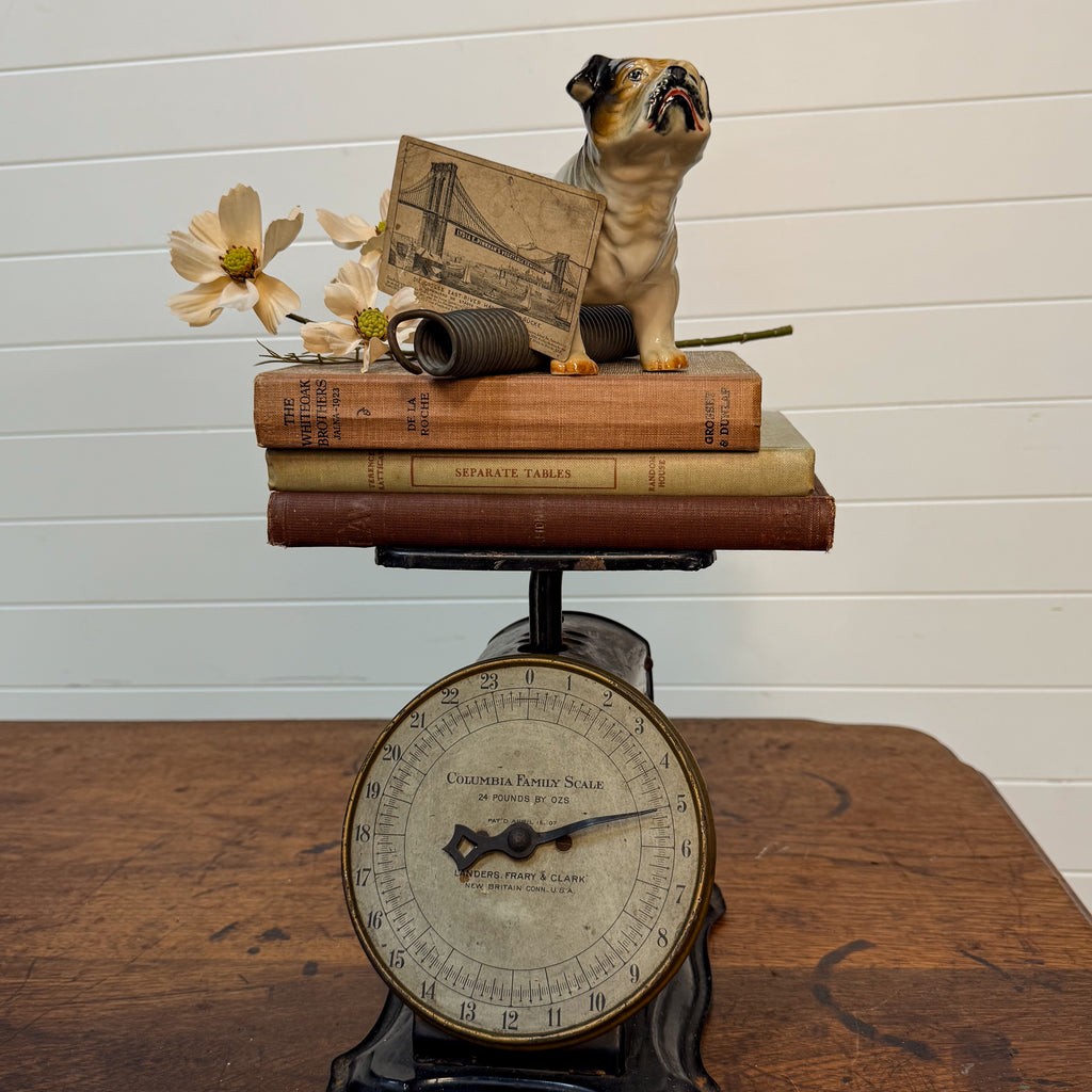 Vintage scale with books and a small dog figurine on top against a white wall.