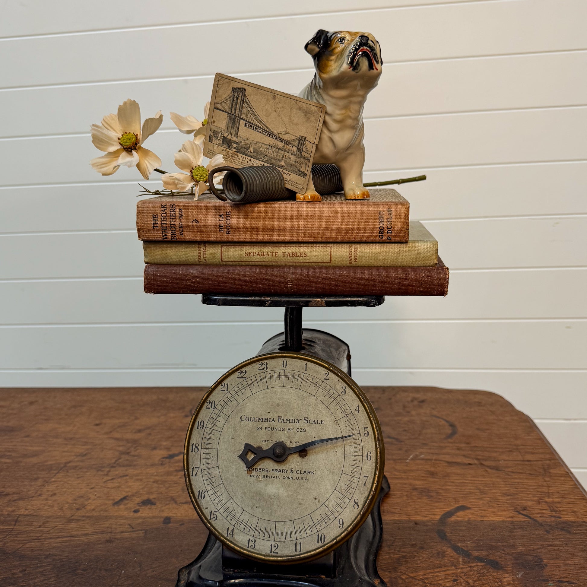 Vintage scale with books and a small dog figurine on top against a white wall.
