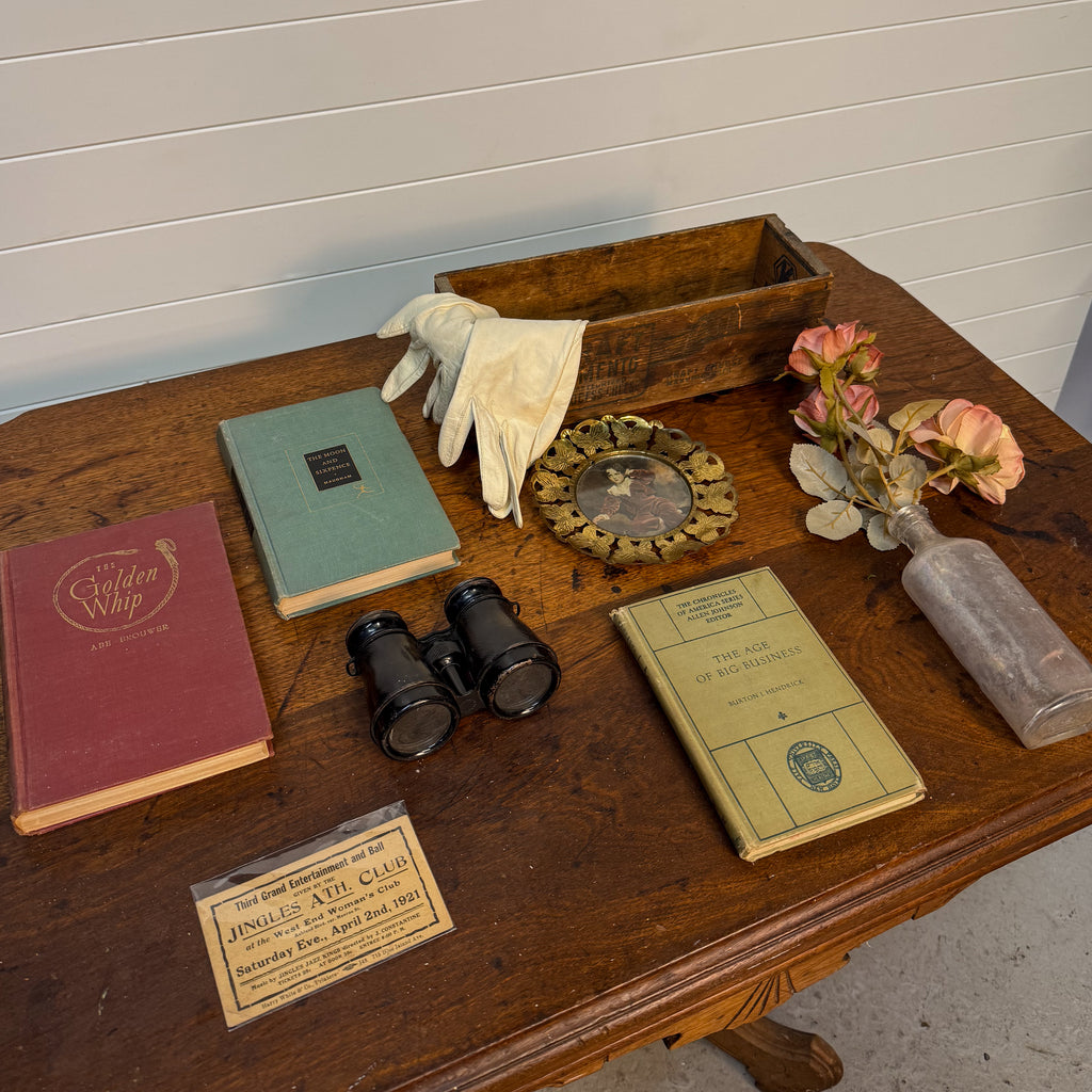Collection of vintage items including books, binoculars, gloves, and a wooden box on a wooden surface.
