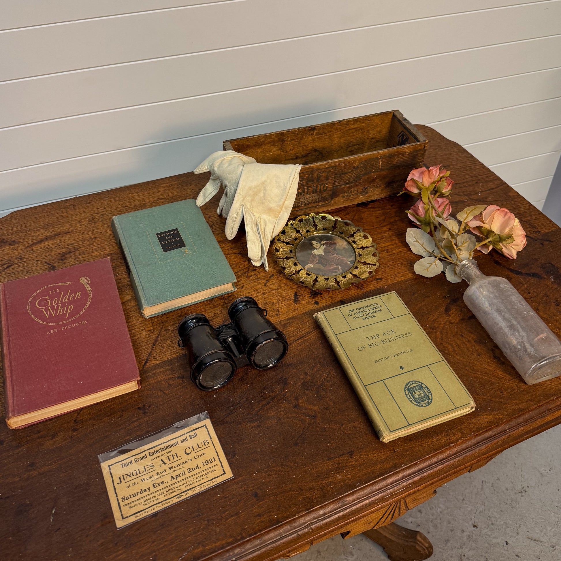 Collection of vintage items including books, binoculars, gloves, and a wooden box on a wooden surface.