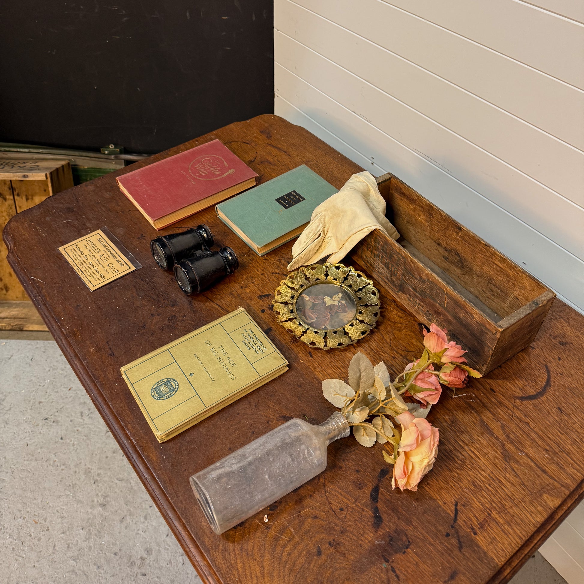 Vintage items including books, binoculars, gloves, and a bottle on a wooden surface.