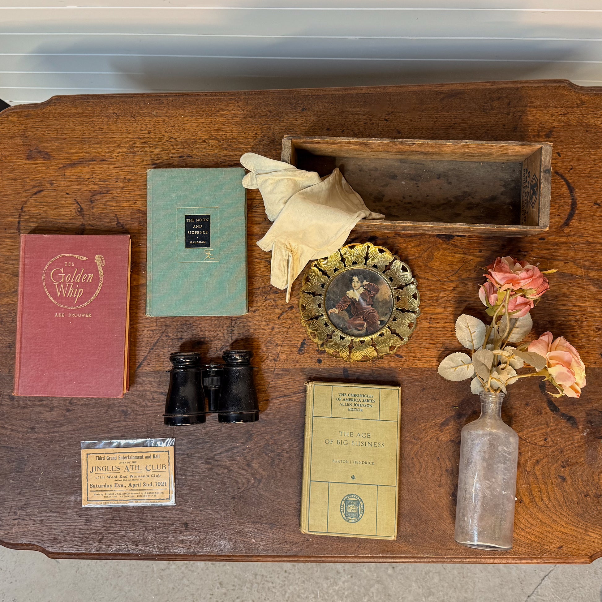 Collection of vintage items on a wooden surface including books, binoculars, and a bottle.