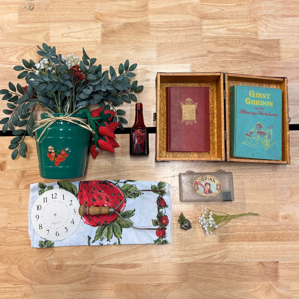 Collection of decorative items including a plant, books, a clock, and a small box on a wooden surface.