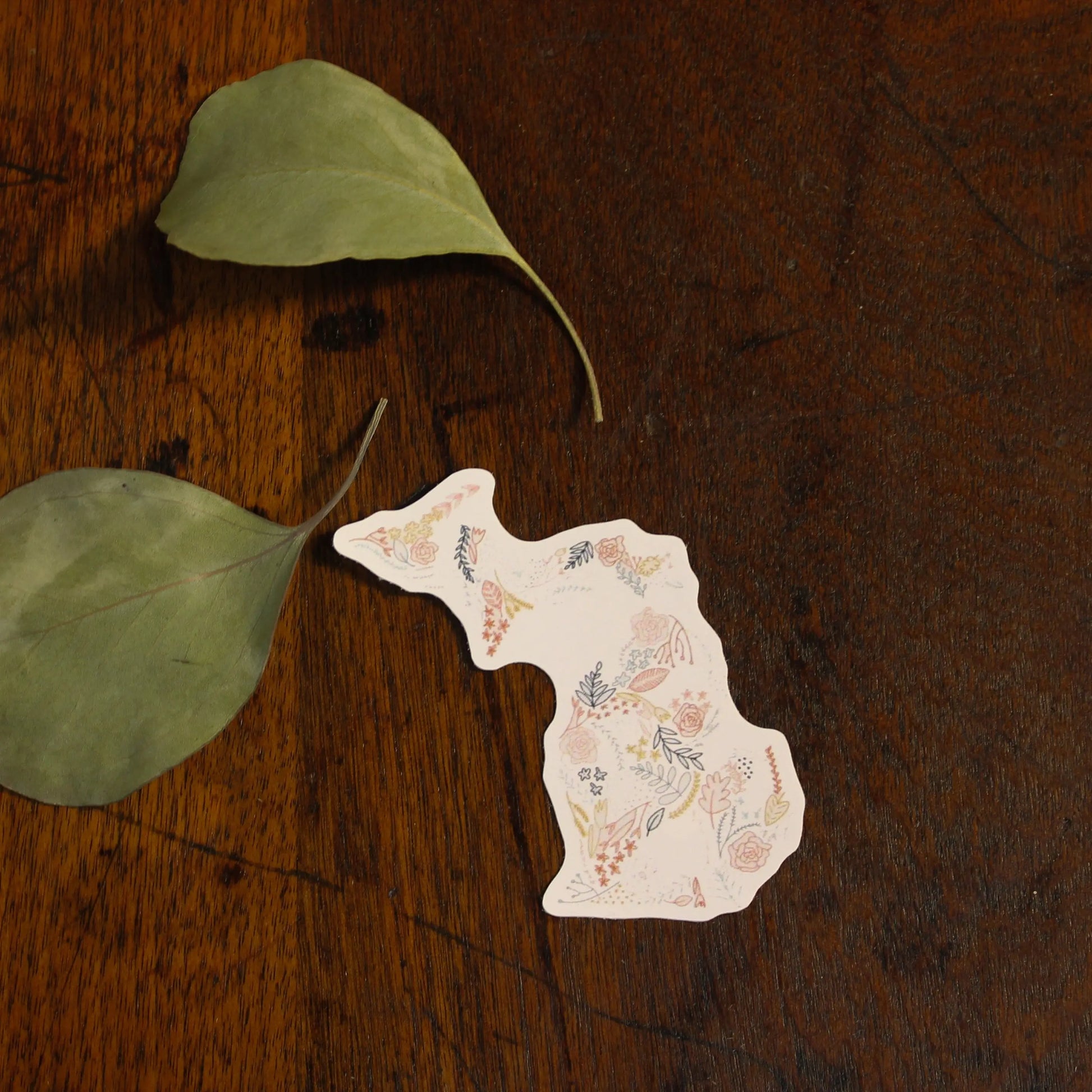 Decorative paper cat with green leaves on a wooden surface