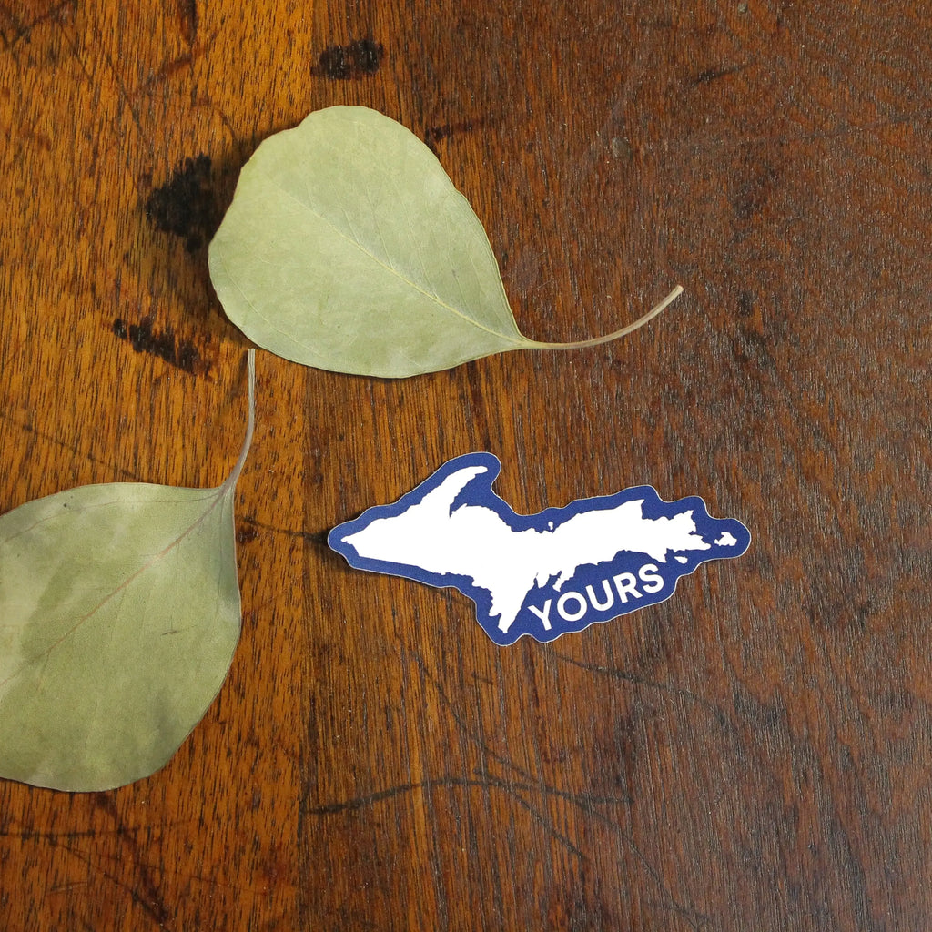 Two green leaves and a blue 'YOURS' sticker on a wooden surface