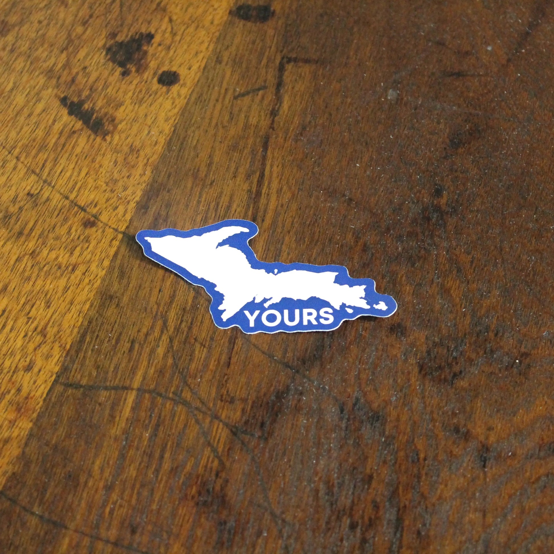 Blue and white sticker with ' U.P. YOURS' text on a wooden surface