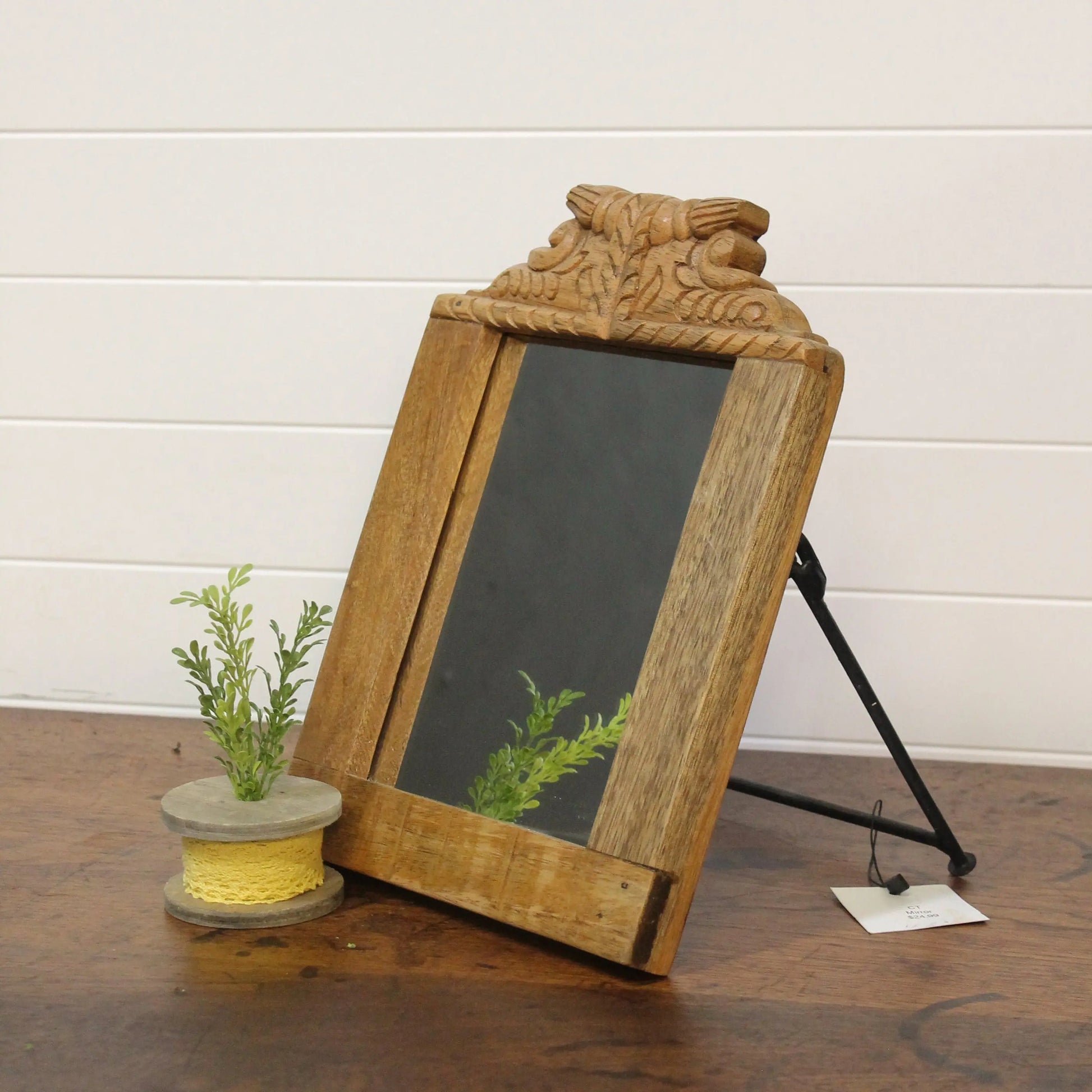Wooden mirror with decorative top on a wooden surface against a white wall.
