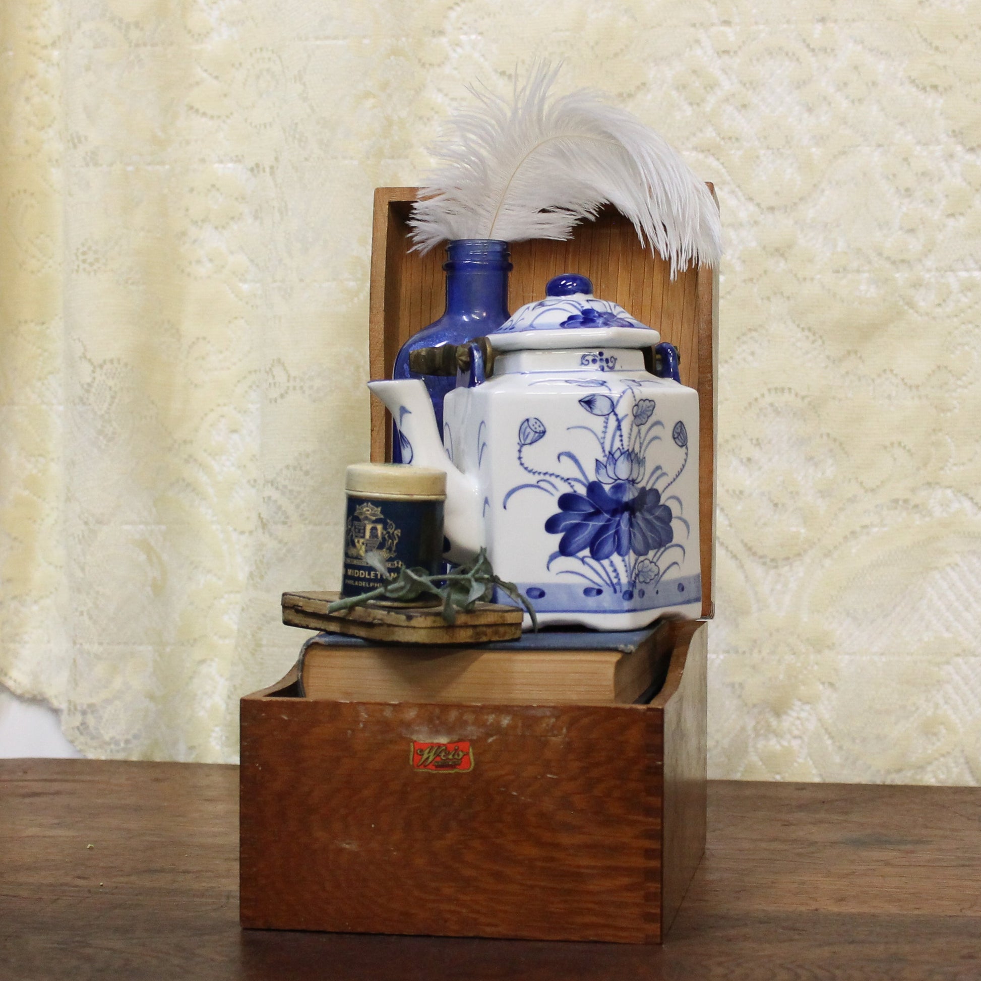 Wooden box with decorative blue and white ceramic jars on a wooden surface with a textured white curtain background.