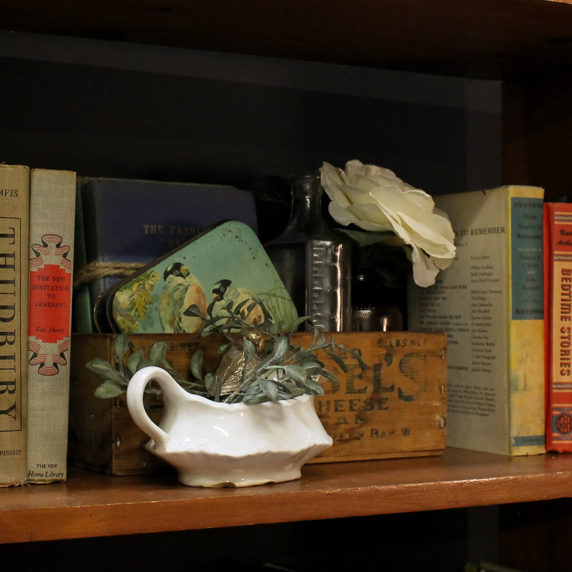Wooden shelf with books, a white pitcher, and decorative items.