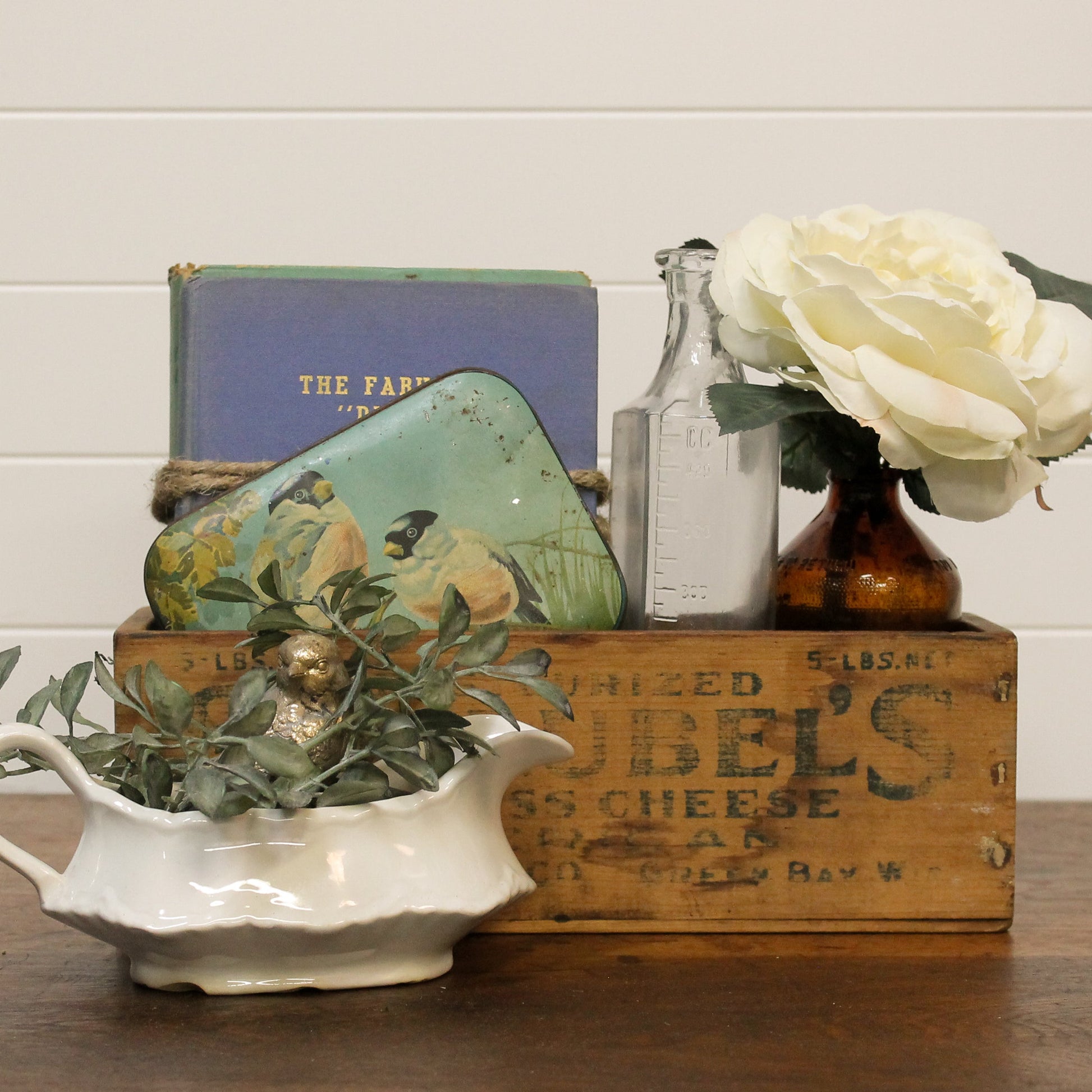 Vintage-style still life arrangement with a box, books, bottles, and flowers on a wooden surface.