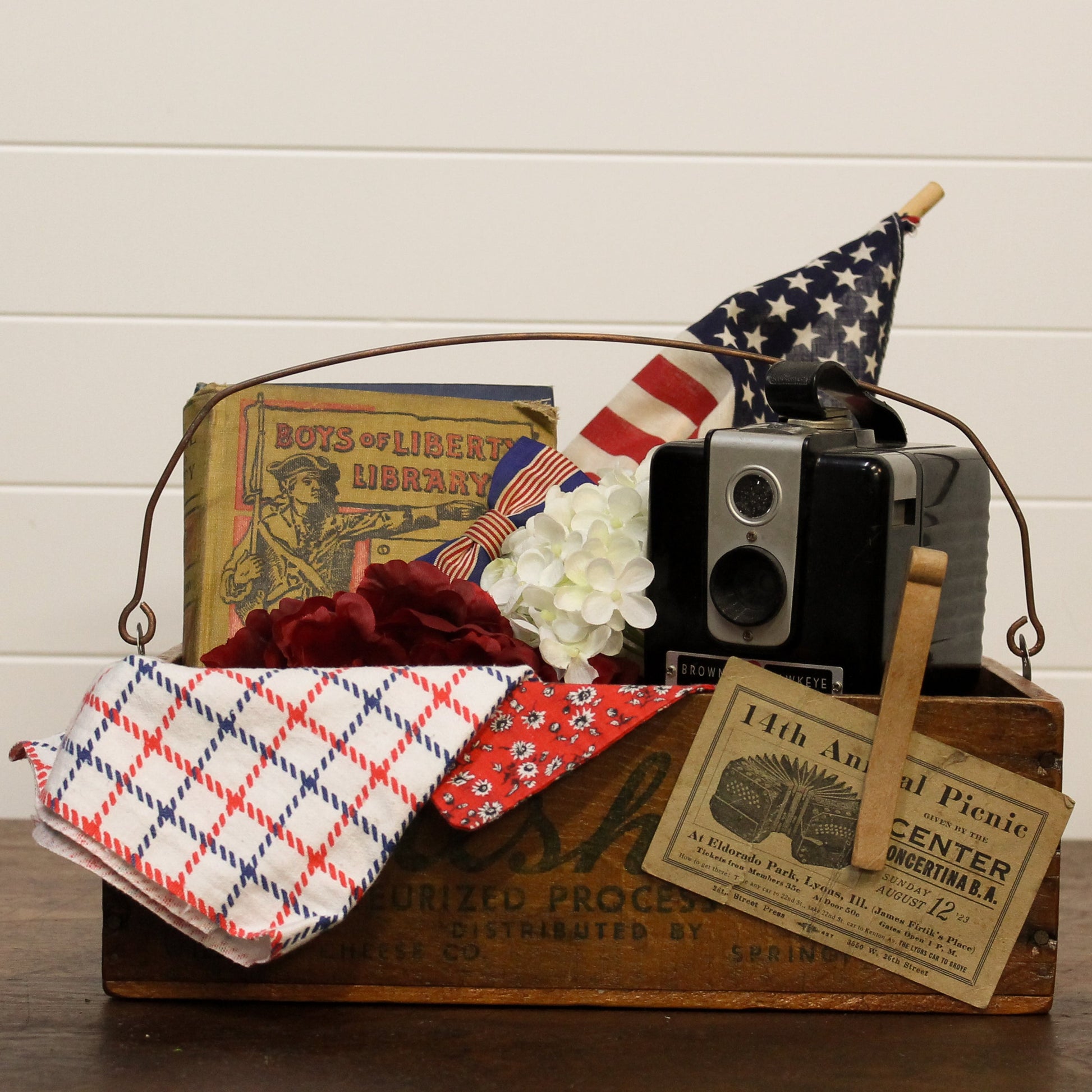 Vintage-style wooden box with patriotic items including a flag, camera, and books on a wooden surface.
