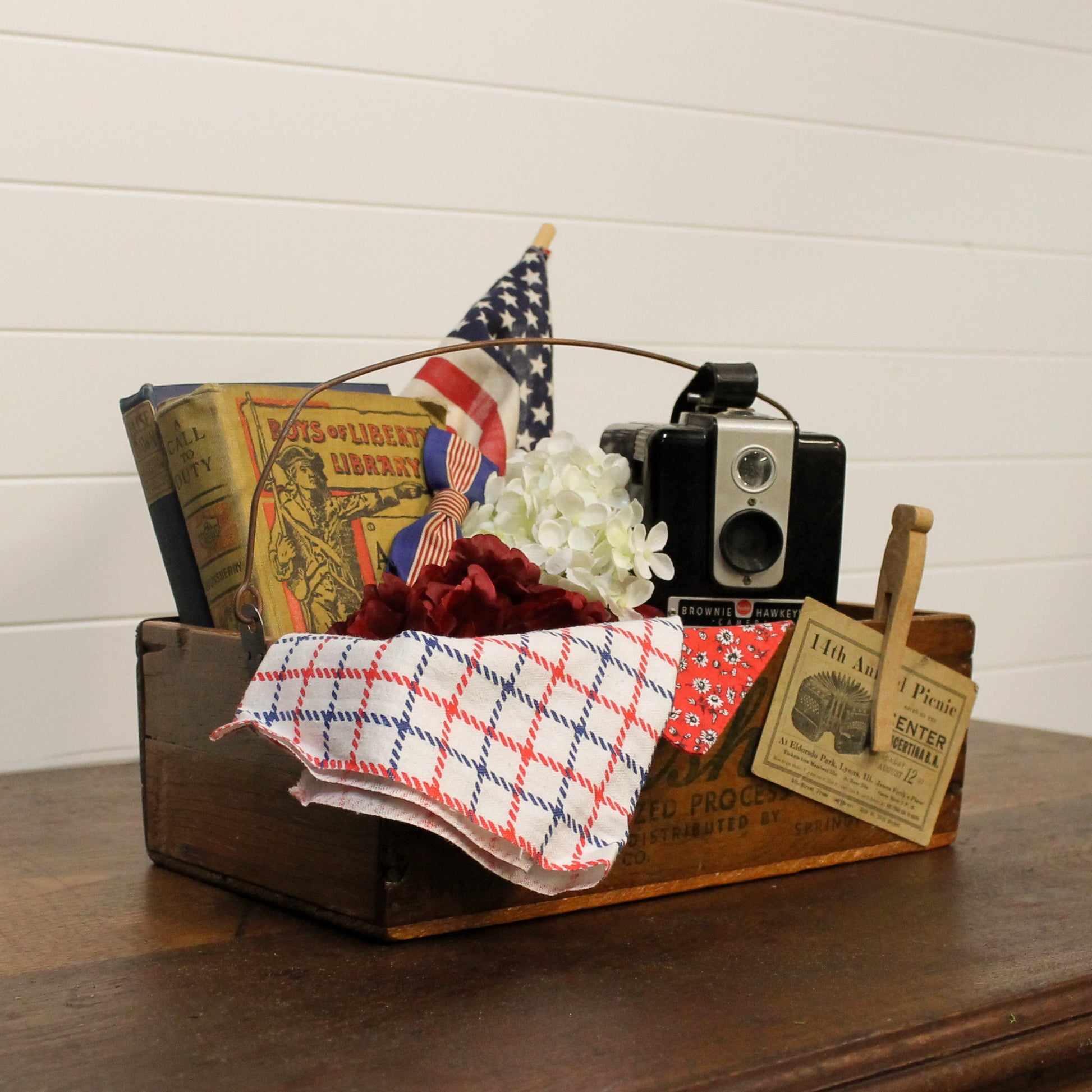 Decorative wooden box with vintage items including a camera, books, and flags on a wooden surface.