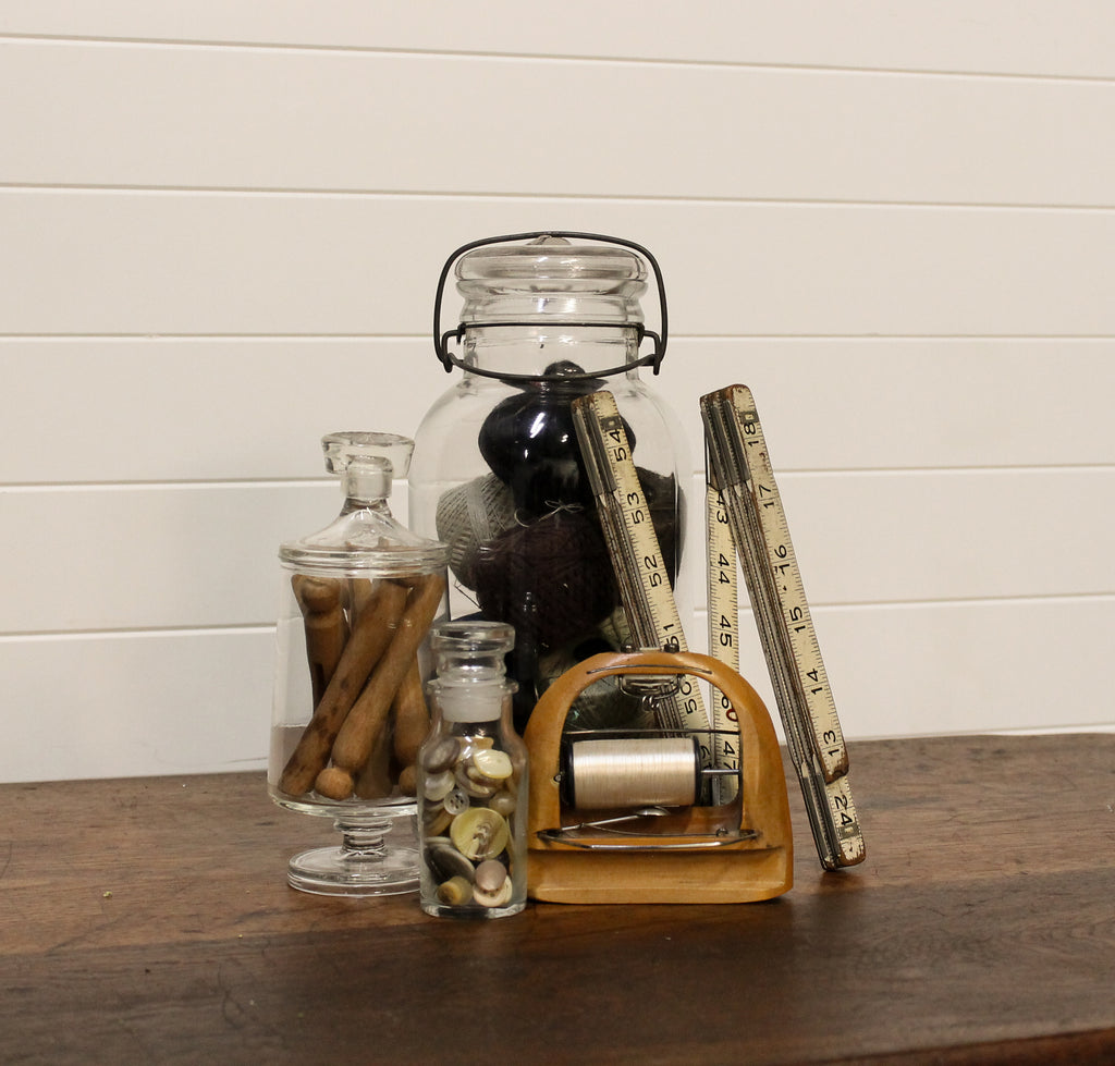 Decorative items including glass jars and a tape measure on a wooden surface with a white paneled wall background.