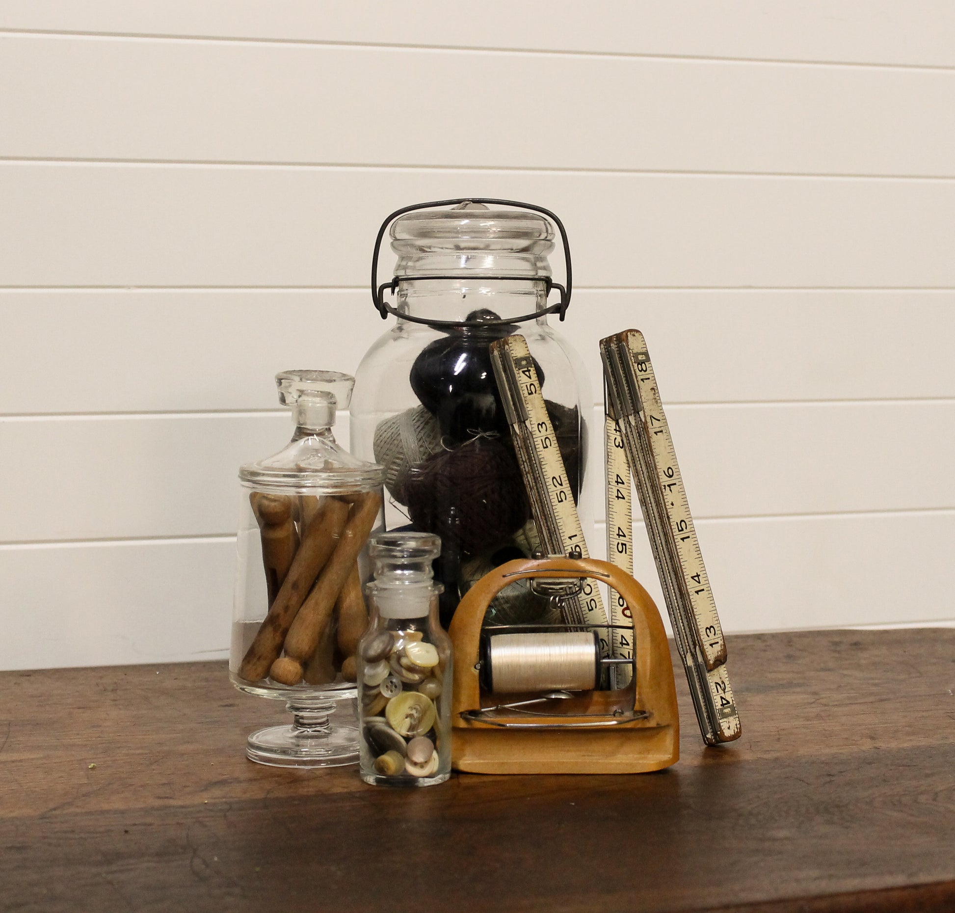 Decorative items including glass jars and a tape measure on a wooden surface with a white paneled wall background.