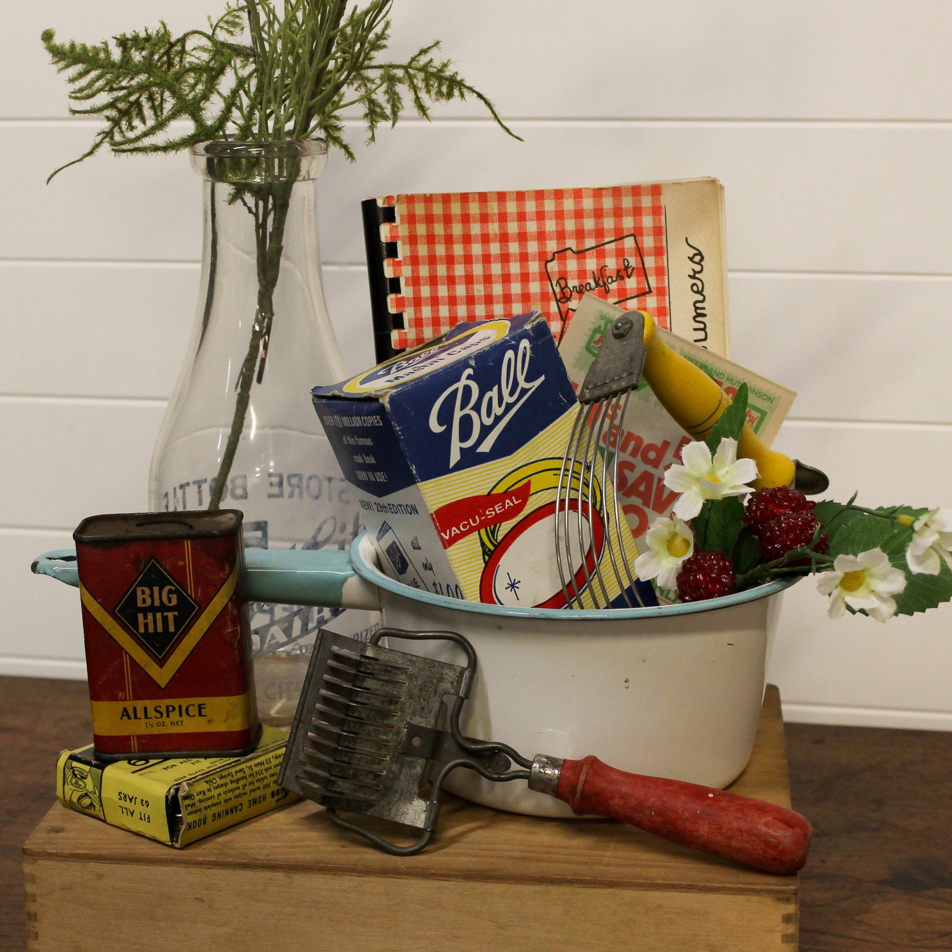 Vintage kitchen items including a can of allspice, a box of Ball brand products, and a grater on a wooden surface.