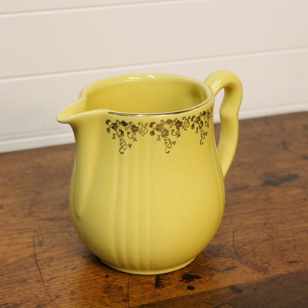 Yellow ceramic pitcher with floral patterns on a wooden surface