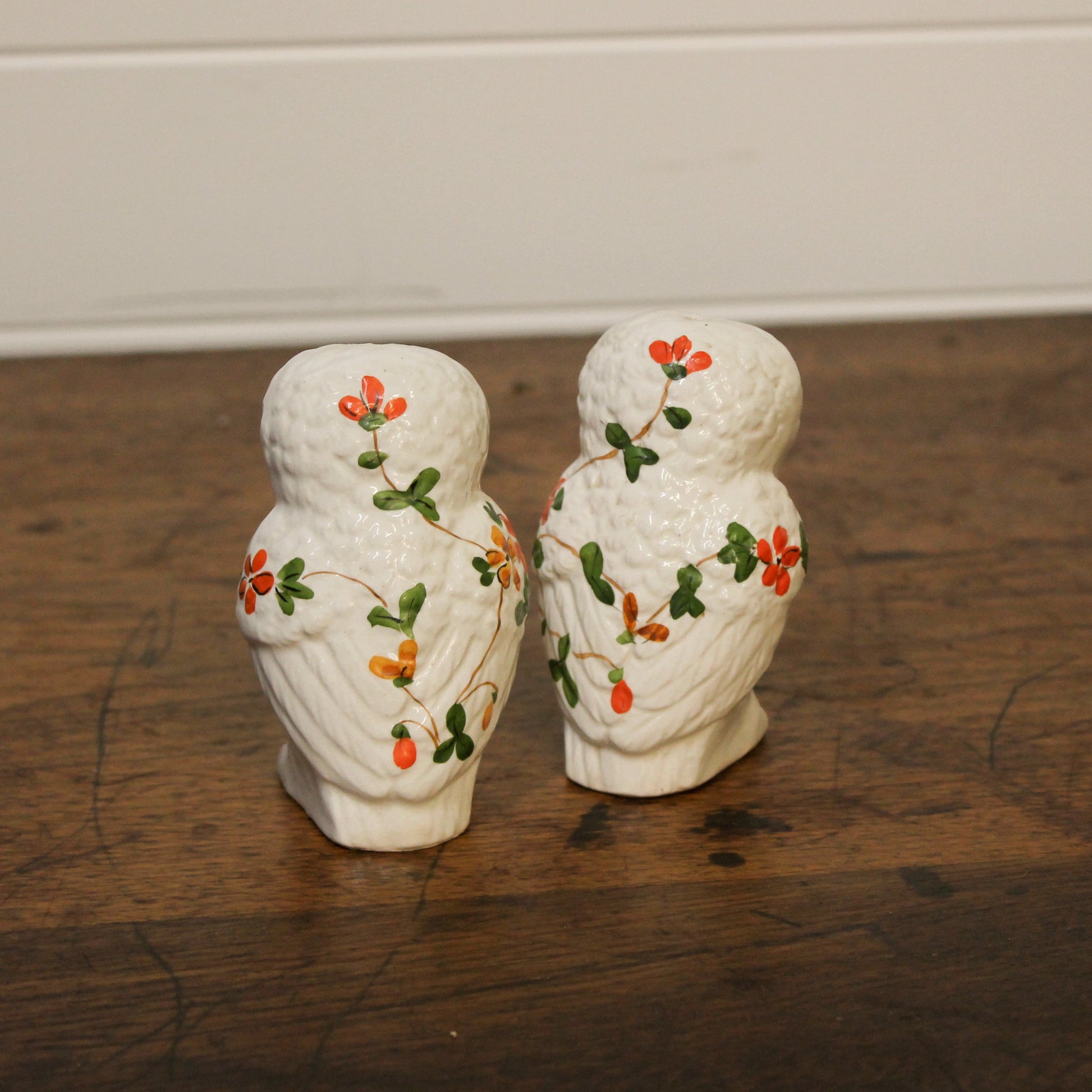 Two white ceramic owls with floral designs on a wooden surface.