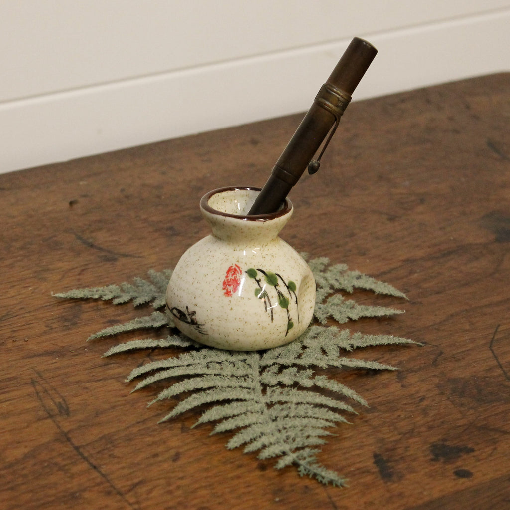 Small ceramic pot with a pen on a wooden surface with a fern leaf