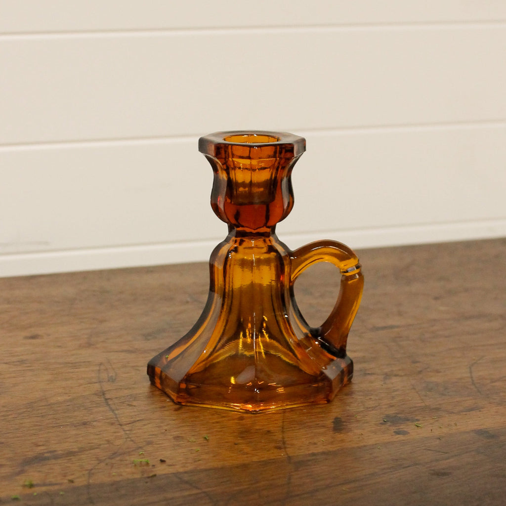 Brown glass candle holder on a wooden surface with a white wall background
