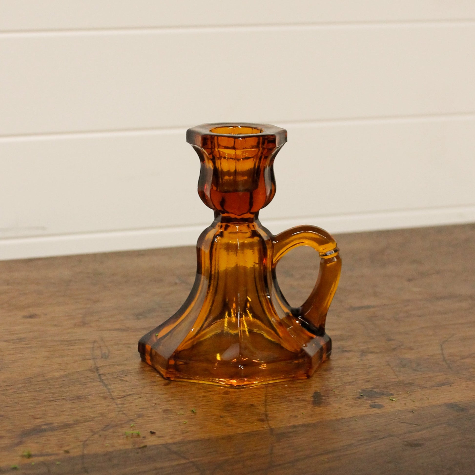 Brown glass candle holder on a wooden surface with a white wall background