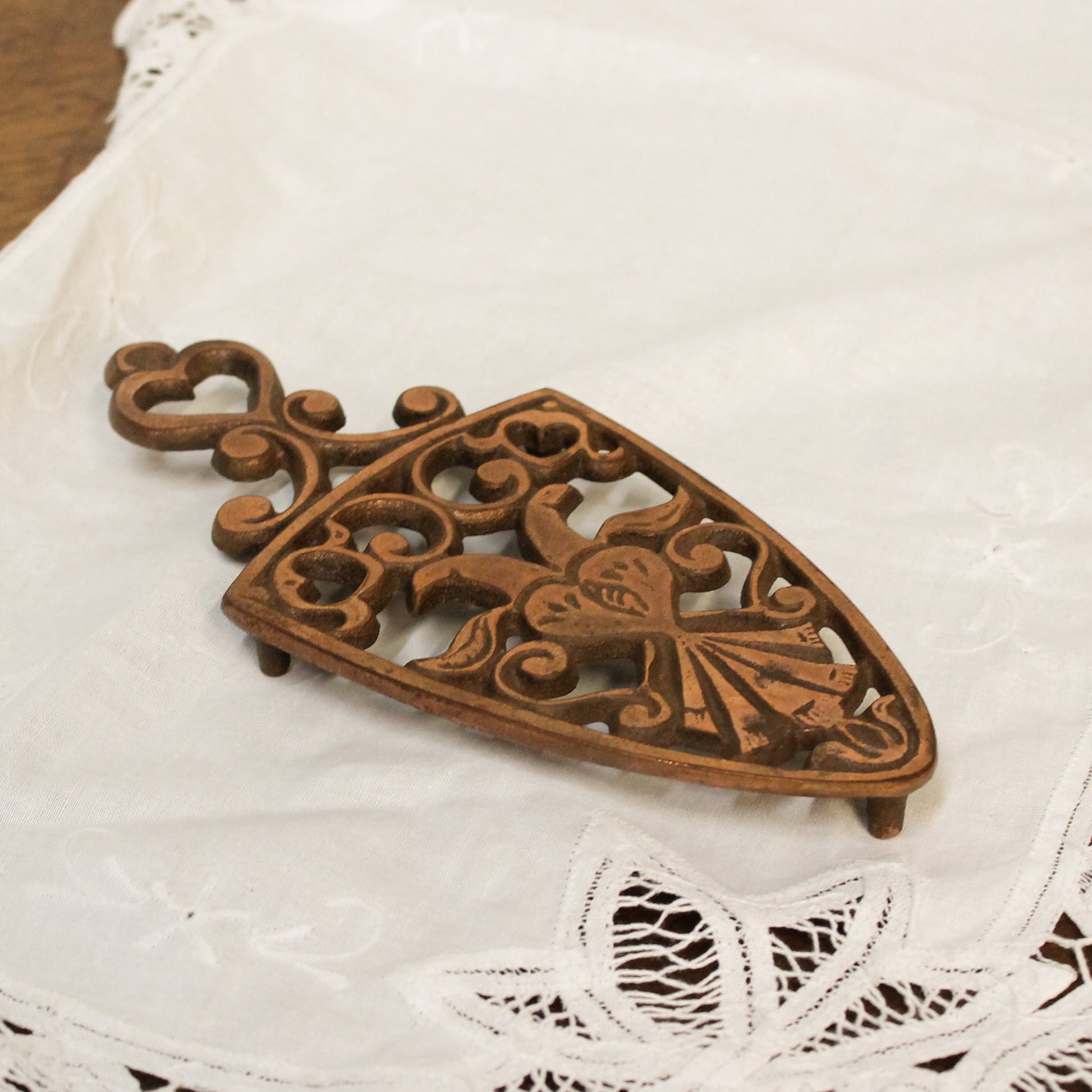 Decorative copper trivet with intricate patterns on a lace tablecloth.