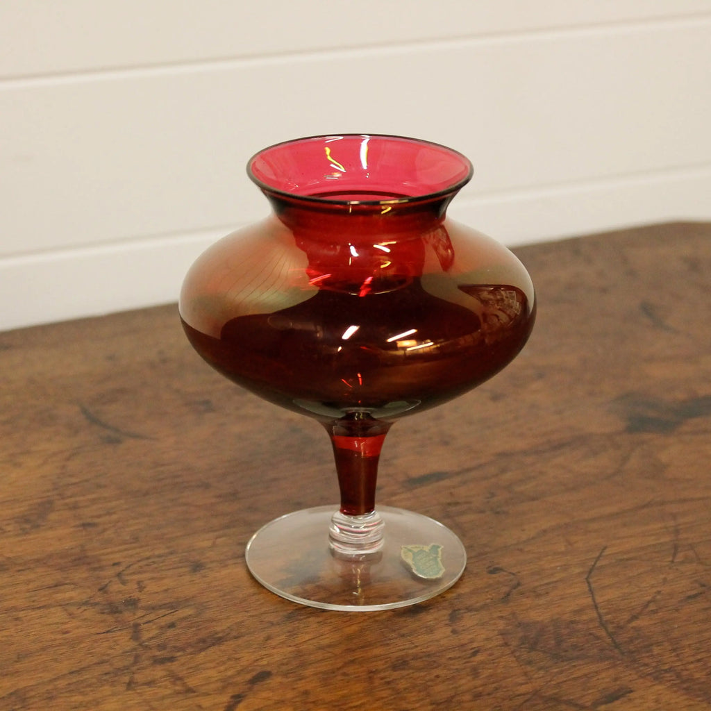 Red glass vase on a wooden surface with a white wall background
