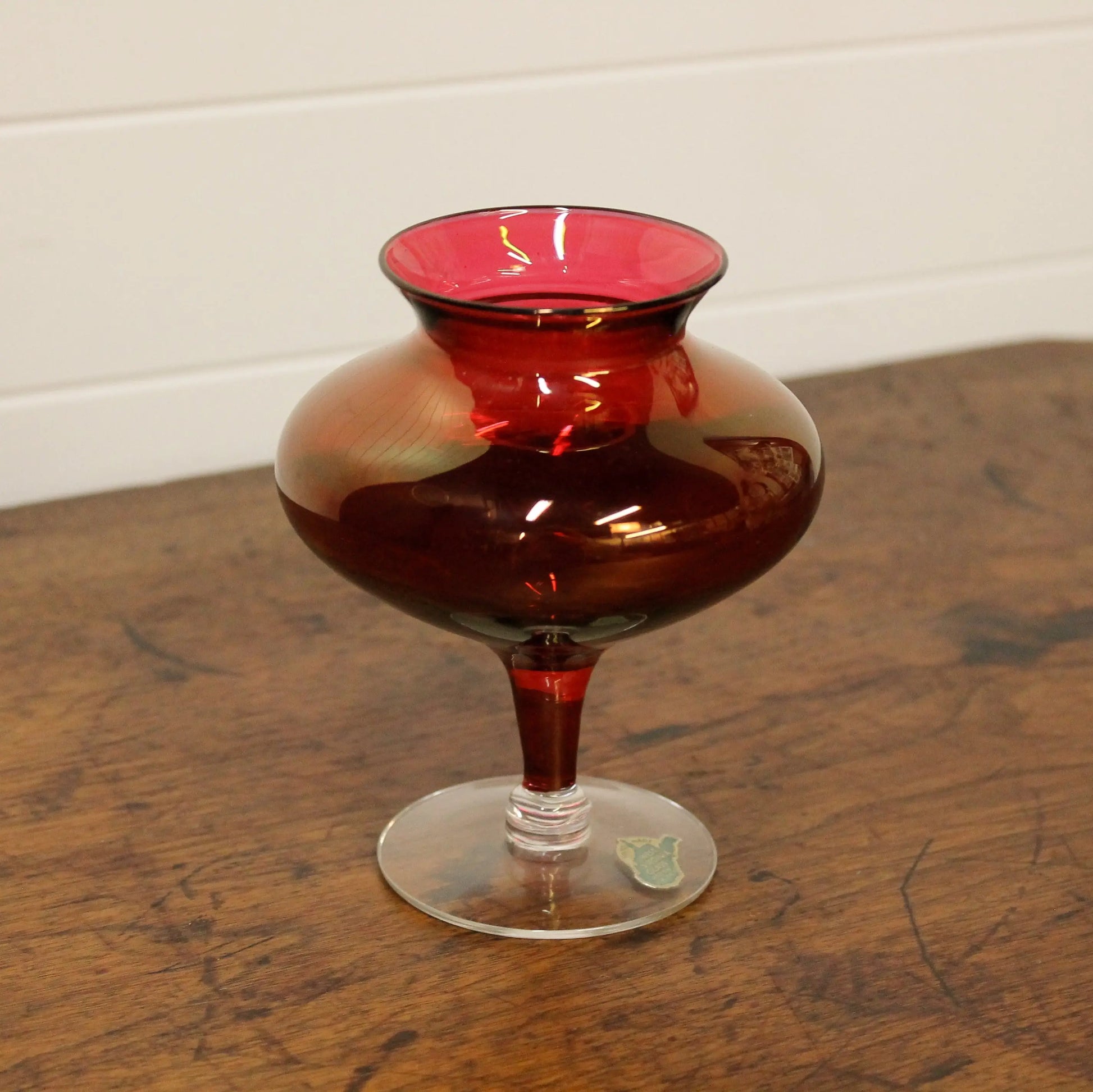 Red glass vase on a wooden surface with a white wall background