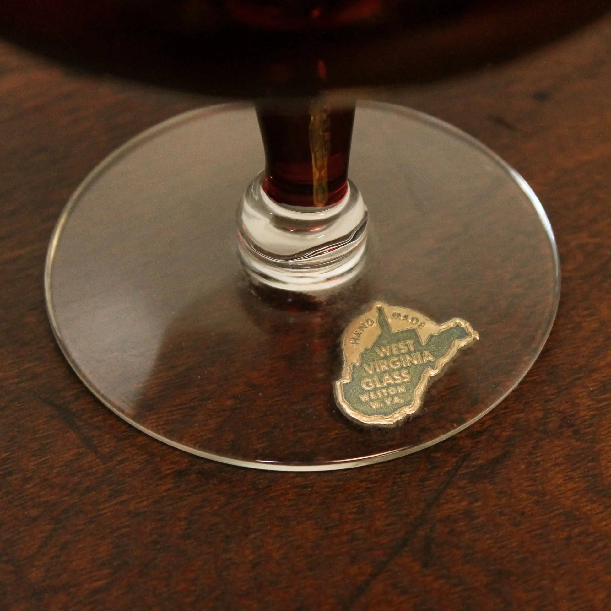 Glass with West Virginia Glass logo on a wooden surface